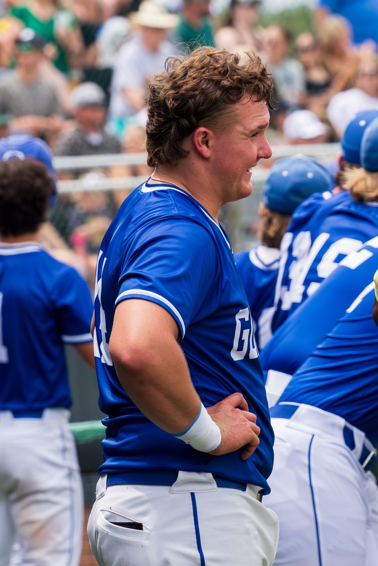 Baseball player in blue Gunter uniform stands in dugout during a competitive game.