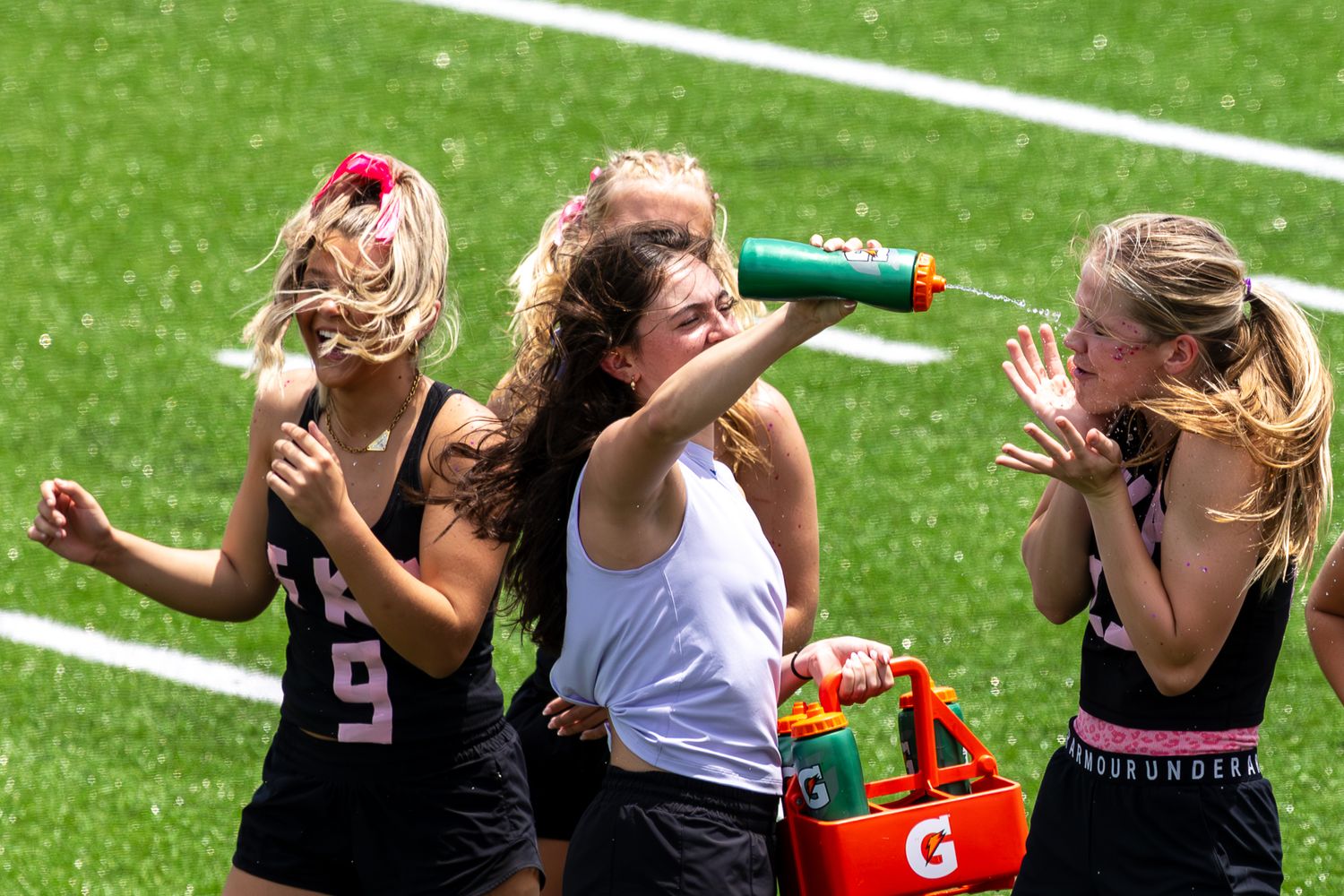 Young female lacrosse players cooling down with Gatorade drinks on a sunny day during a sports tournament.