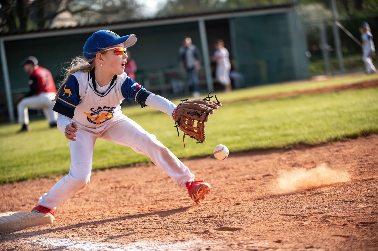 Young girl stretches to catch a ball at first base during a youth softball game.
