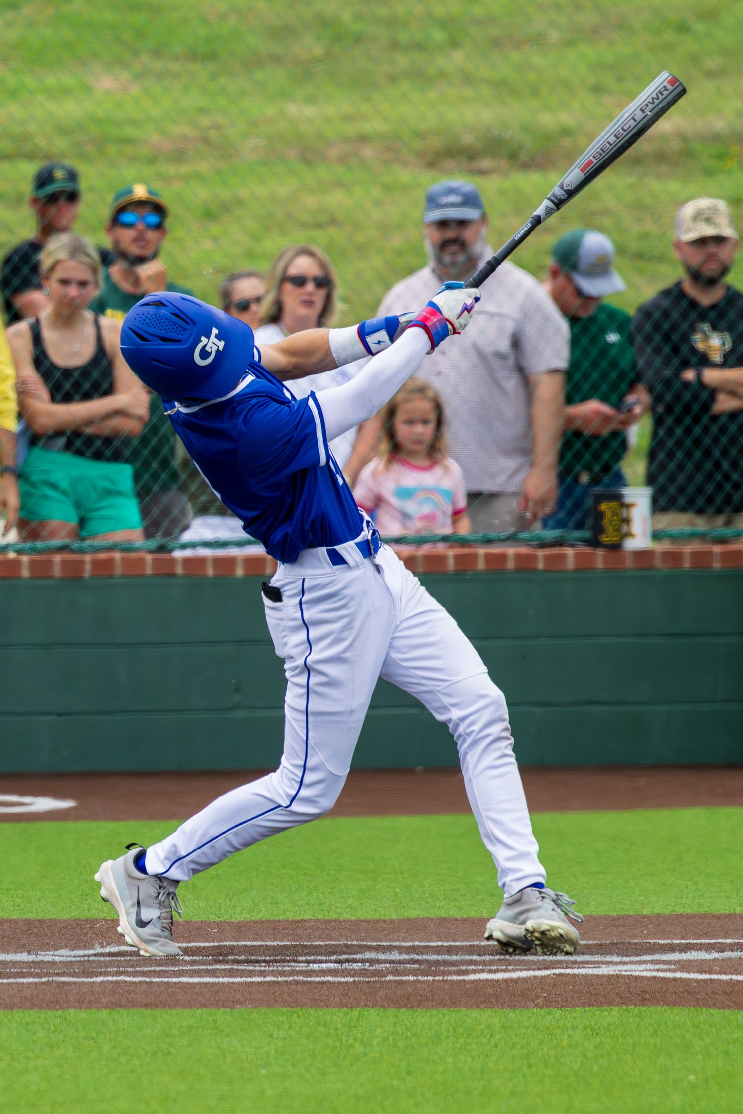 Baseball player in blue uniform swinging bat during a game with fans watching in the background.