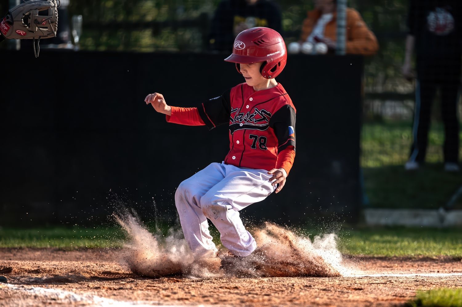 Young baseball player slides into home plate in a cloud of dirt during a little league game.
