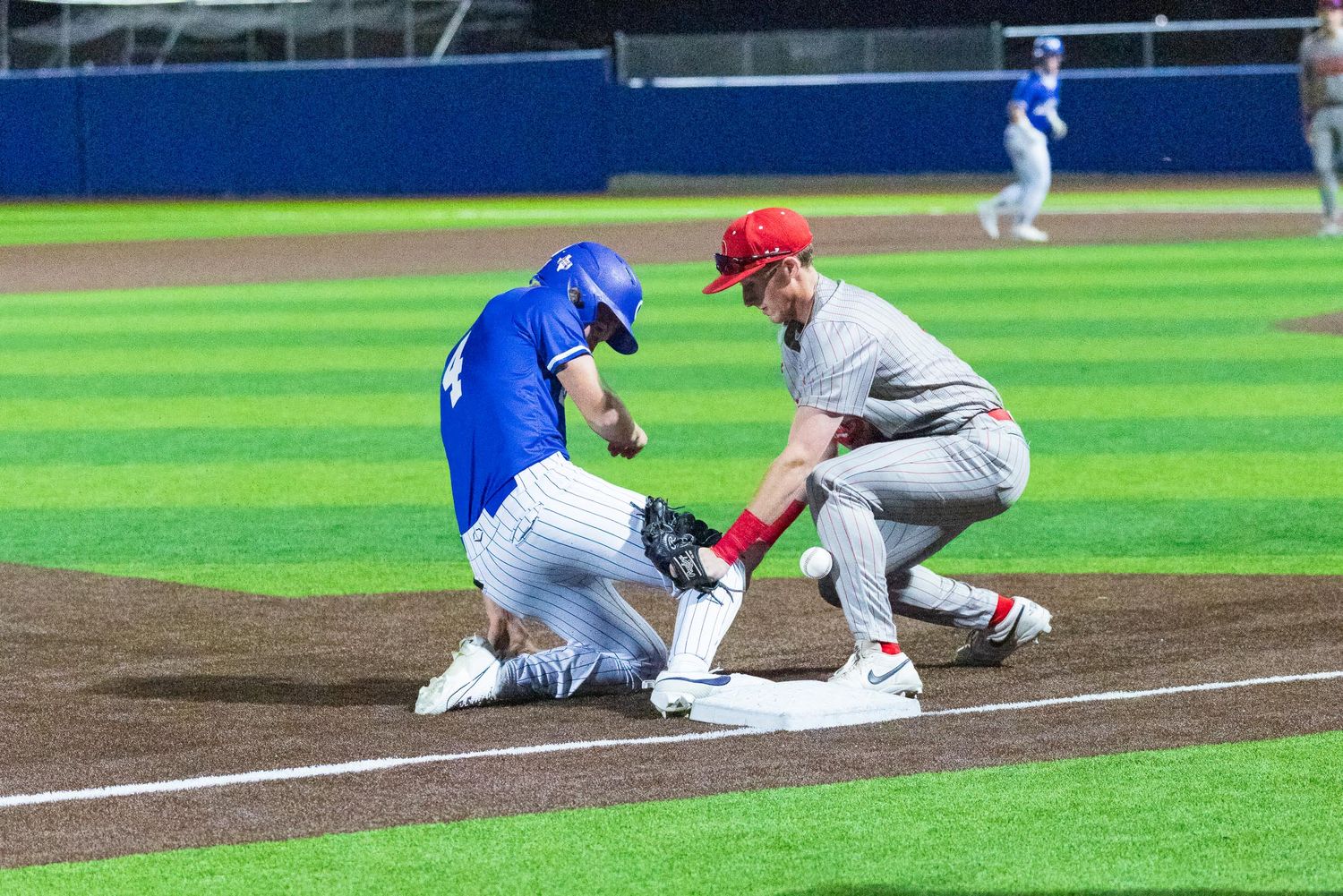 Baseball player in red tags out sliding runner in blue uniform at third base during night game. Gunter Baseball Gunter ISD