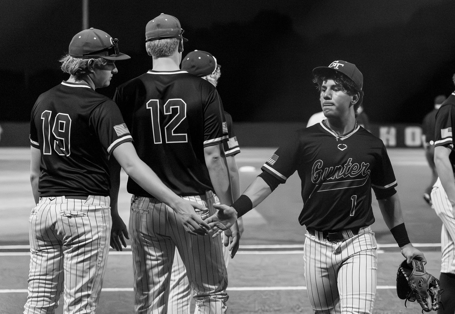 Baseball players in black and white uniforms exchange handshakes on field after a game, wearing numbers 19 and 12.