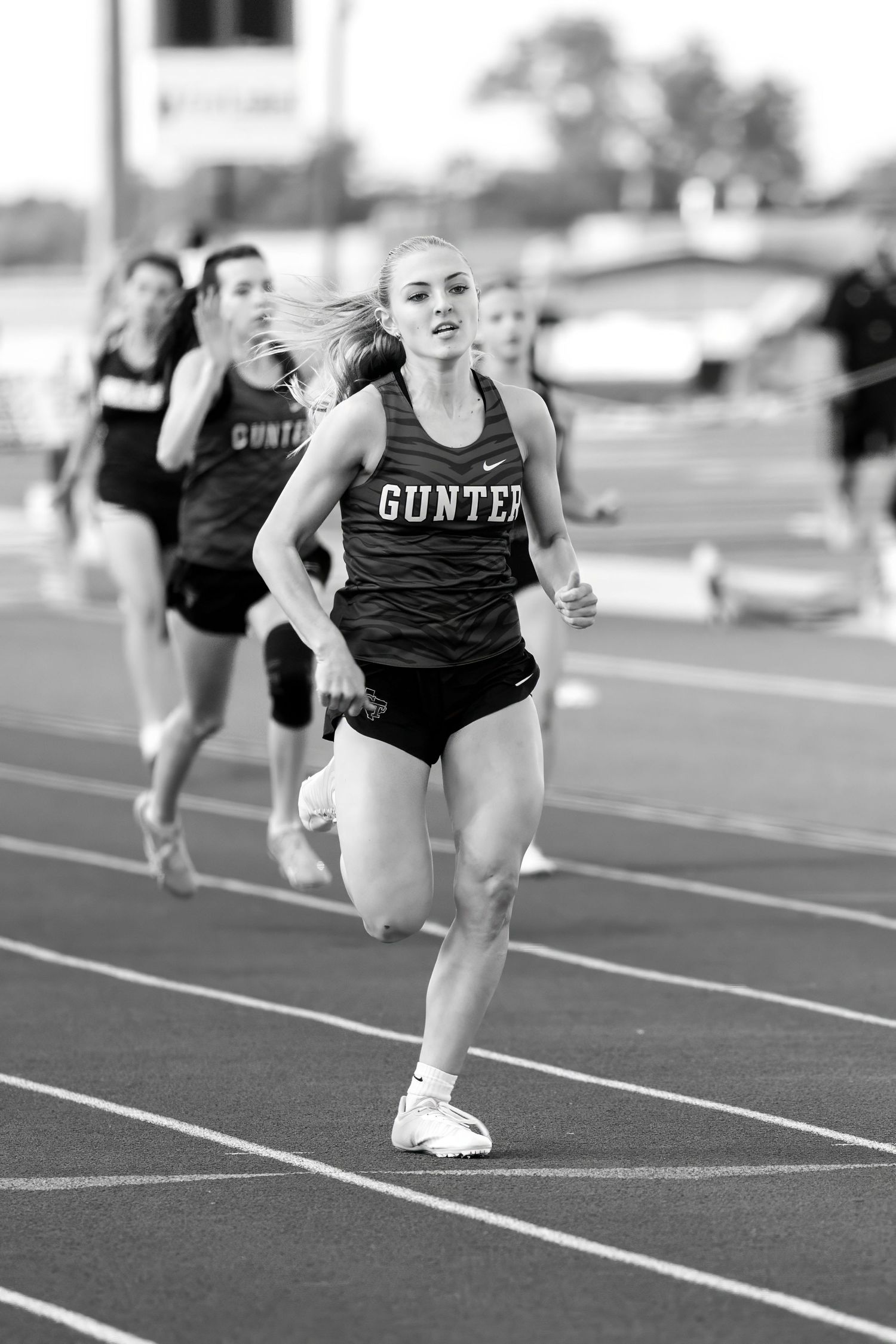 Black and white photo of a Gunter female athlete leading a pack of runners on the track.