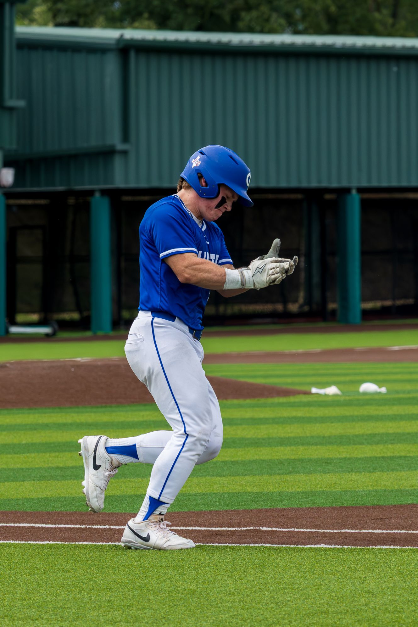 Baseball player in blue uniform celebrating while running the bases during a college baseball game.