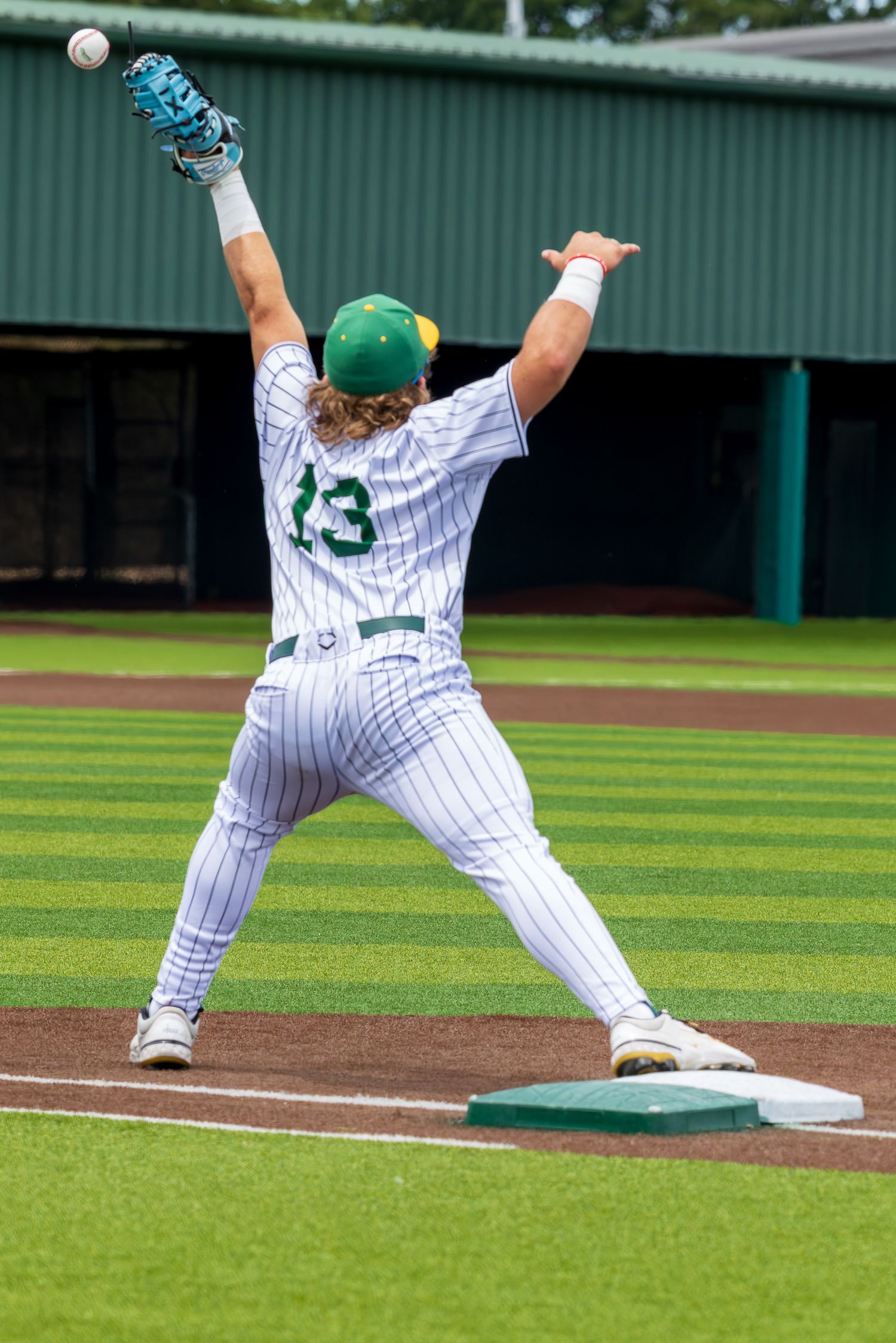 Baseball first baseman in white pinstripe uniform number 13 stretches to catch a throw during a game.