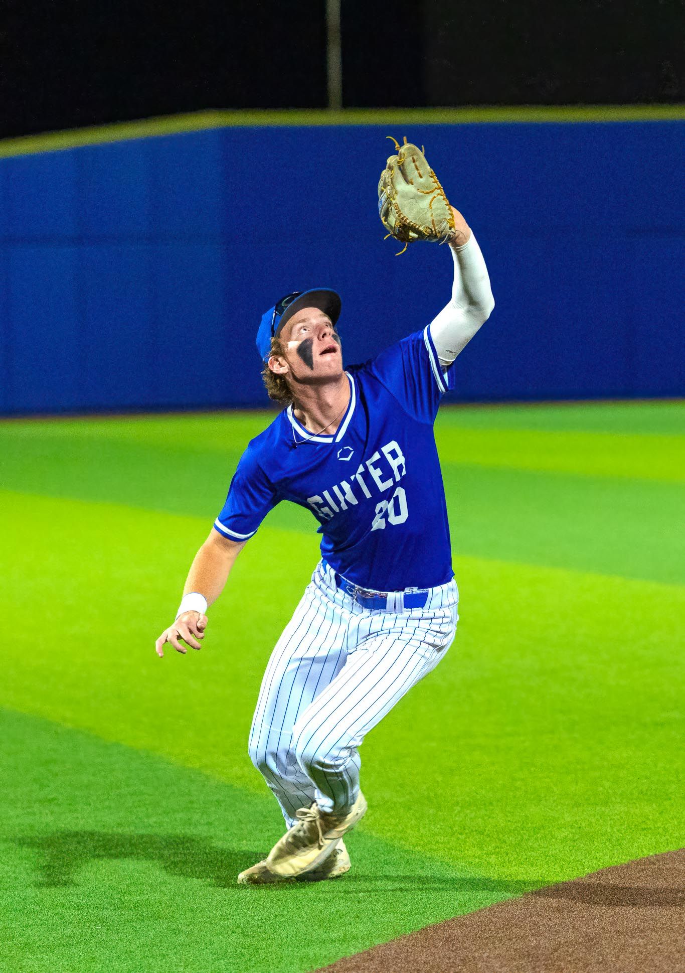 Baseball player in blue uniform catches a fly ball on the field during a night game.