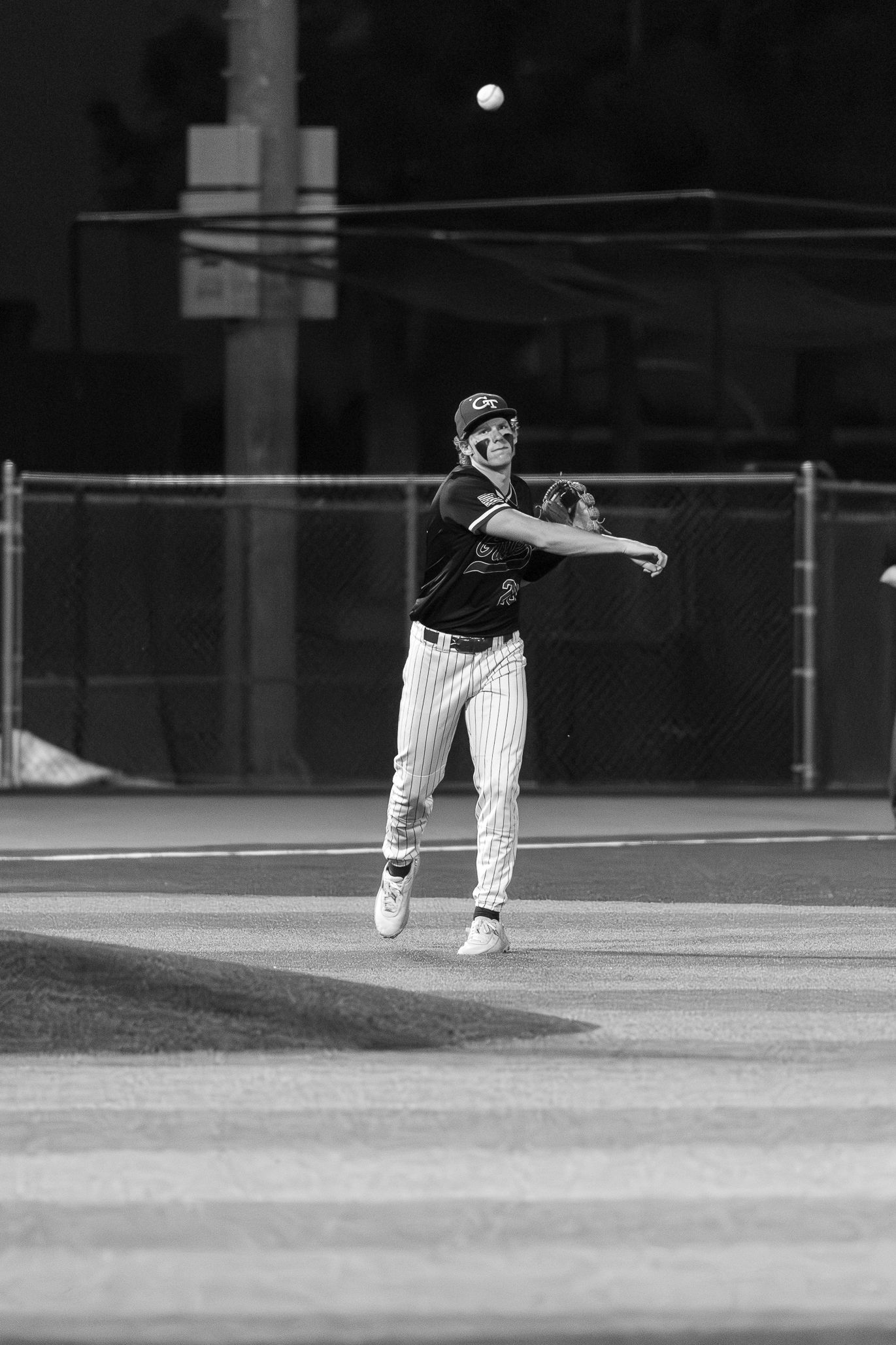 Black and white photo of a baseball player throwing the ball during a night game on the field.