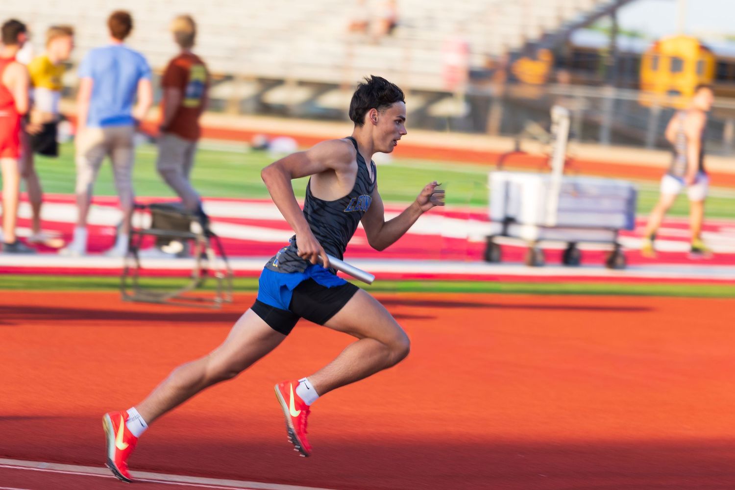 Young male athlete sprints powerfully around the track during a competitive track and field meet.