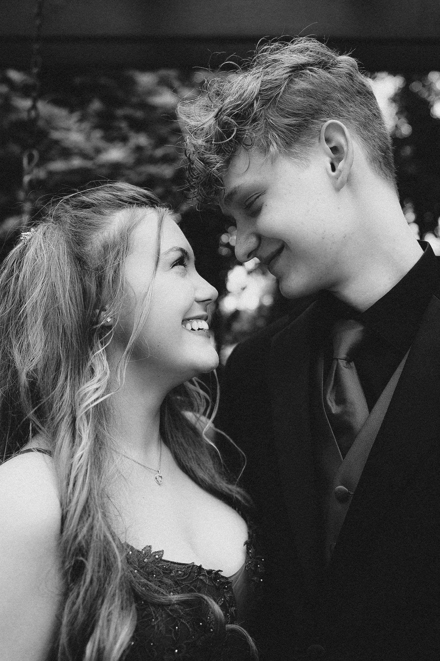 Black and white photo of a smiling young couple in formal attire gazing at each other at prom.