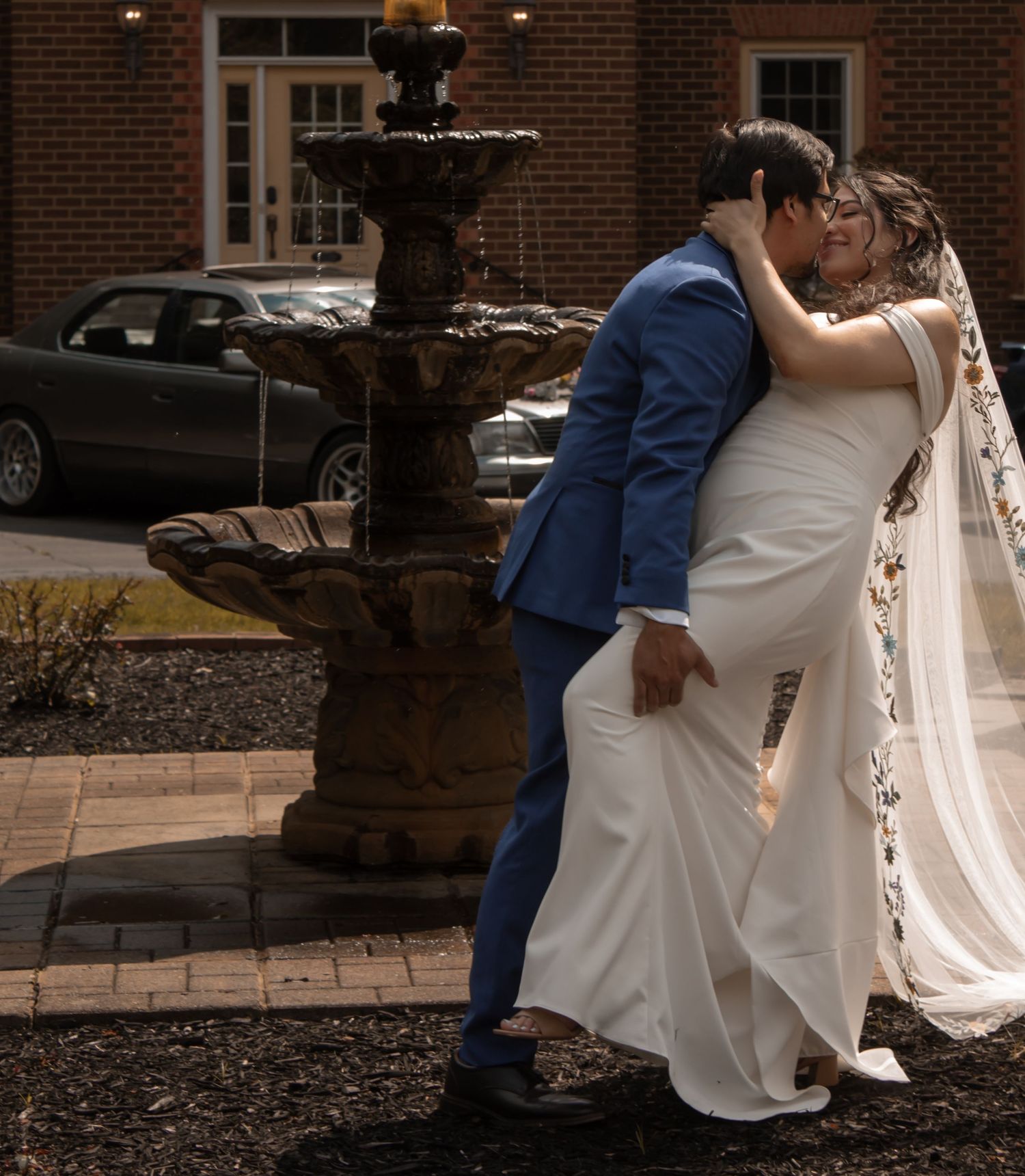 picture of bride and groom near fountain. Groom dipping bride slightly while hold her leg. bride is smiling
