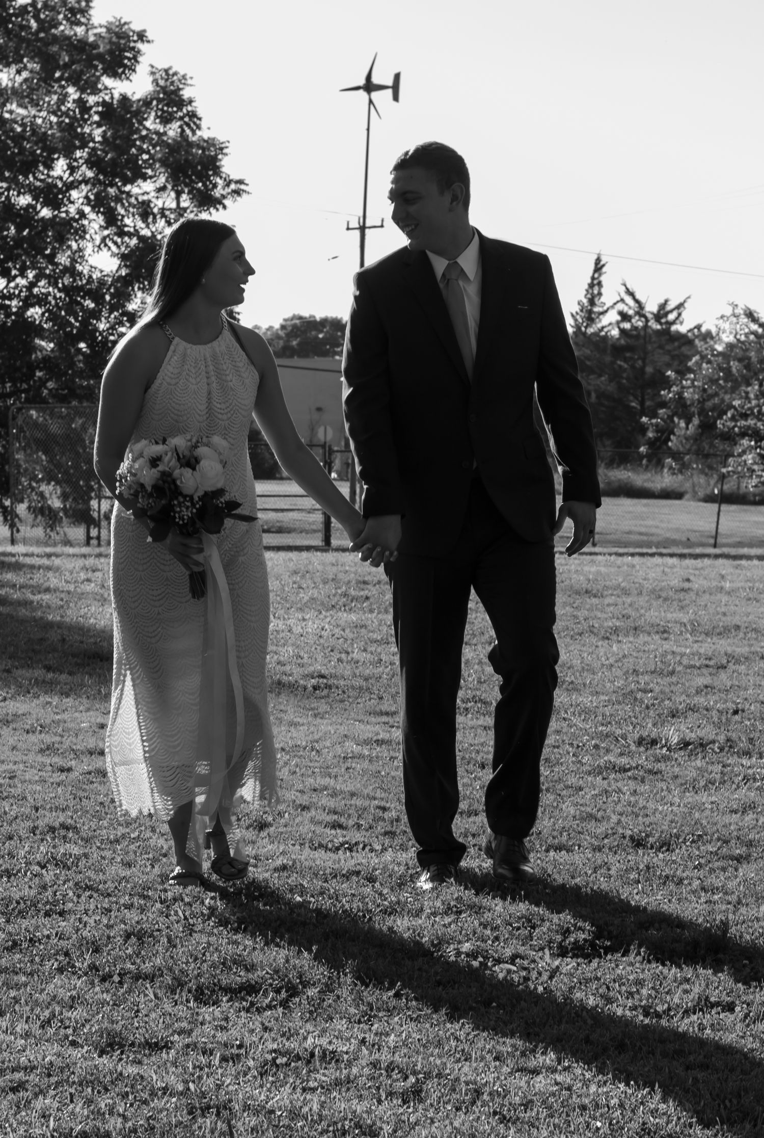 black and white picture of couple walking together. bride holding on to her bouquet, they are both looking at each other.