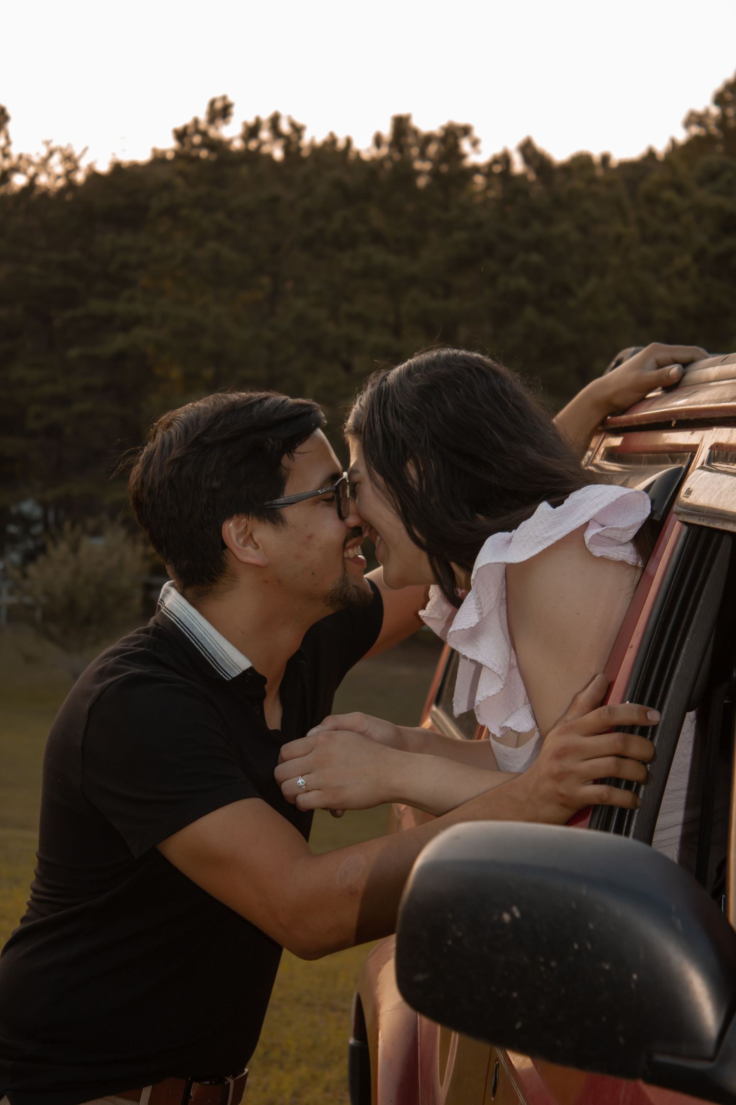 picture of couple, engagement,  girl in the car, sticking out of window and the guy is standing outside the car and they're about to kiss
