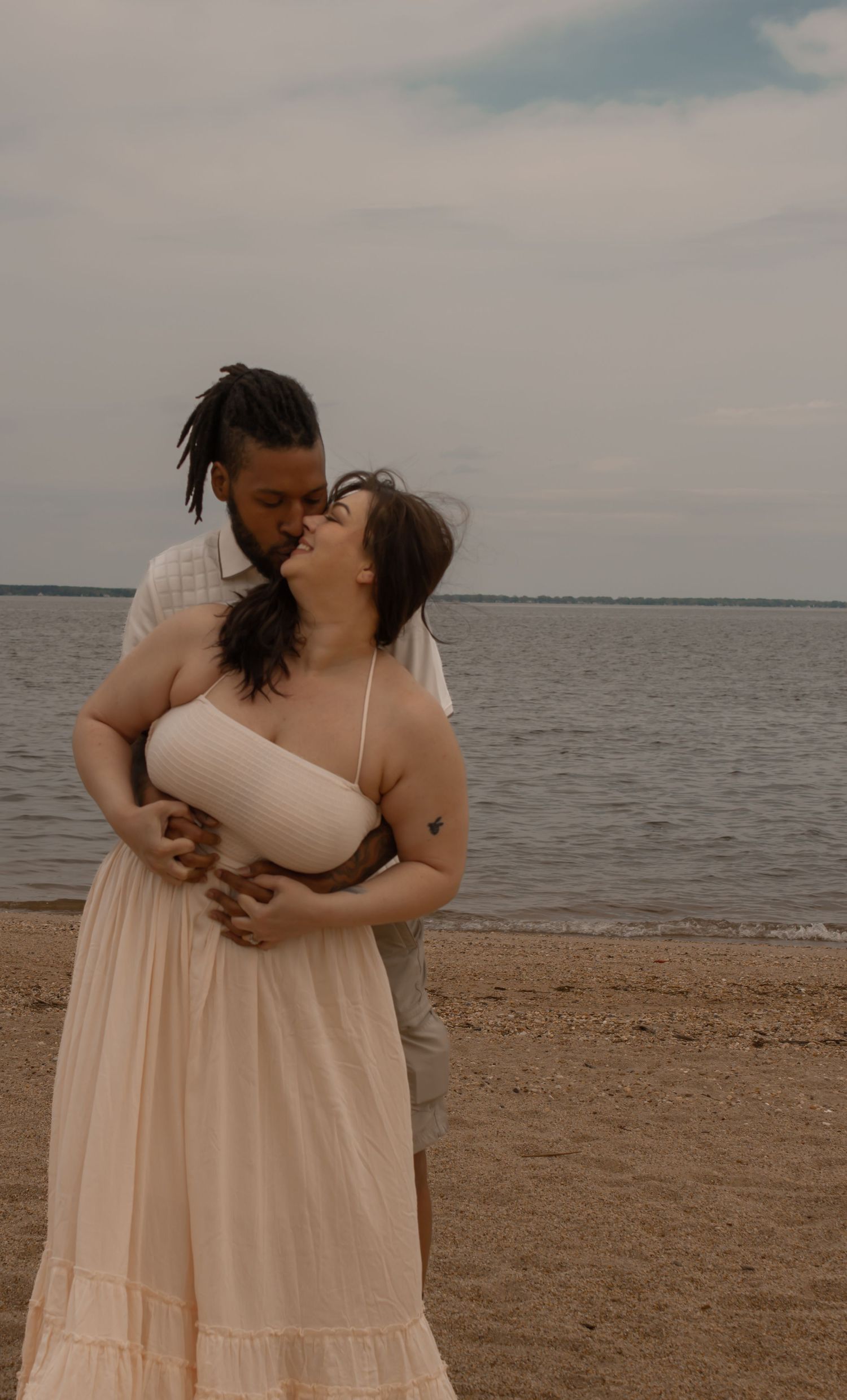 picture of couple on beach, guy holding girl from the back, girl is looking up and smiling while he kisses her.
