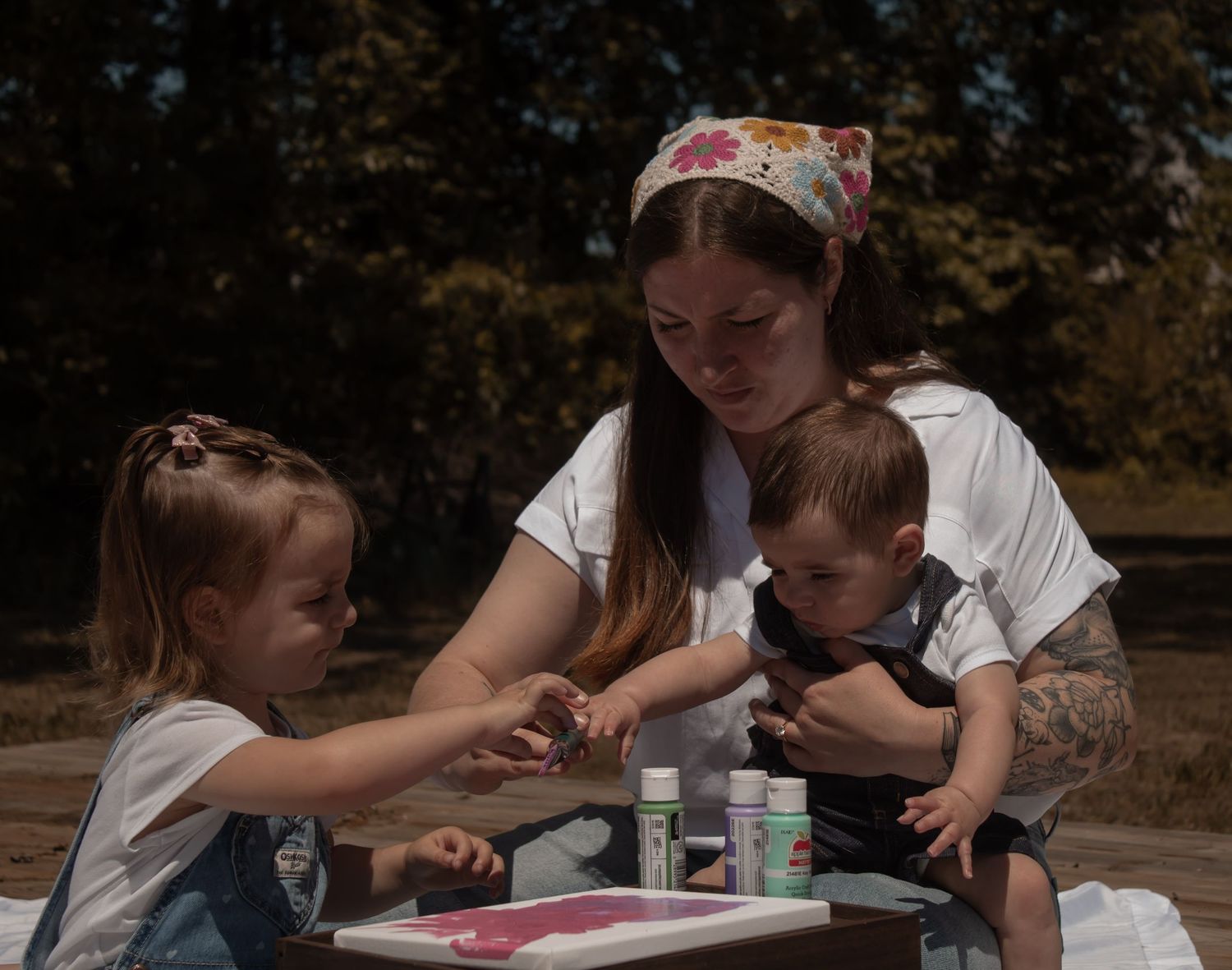 picture of mommy and me session, mom and holding baby boy while helping toddler daughter with the painting.