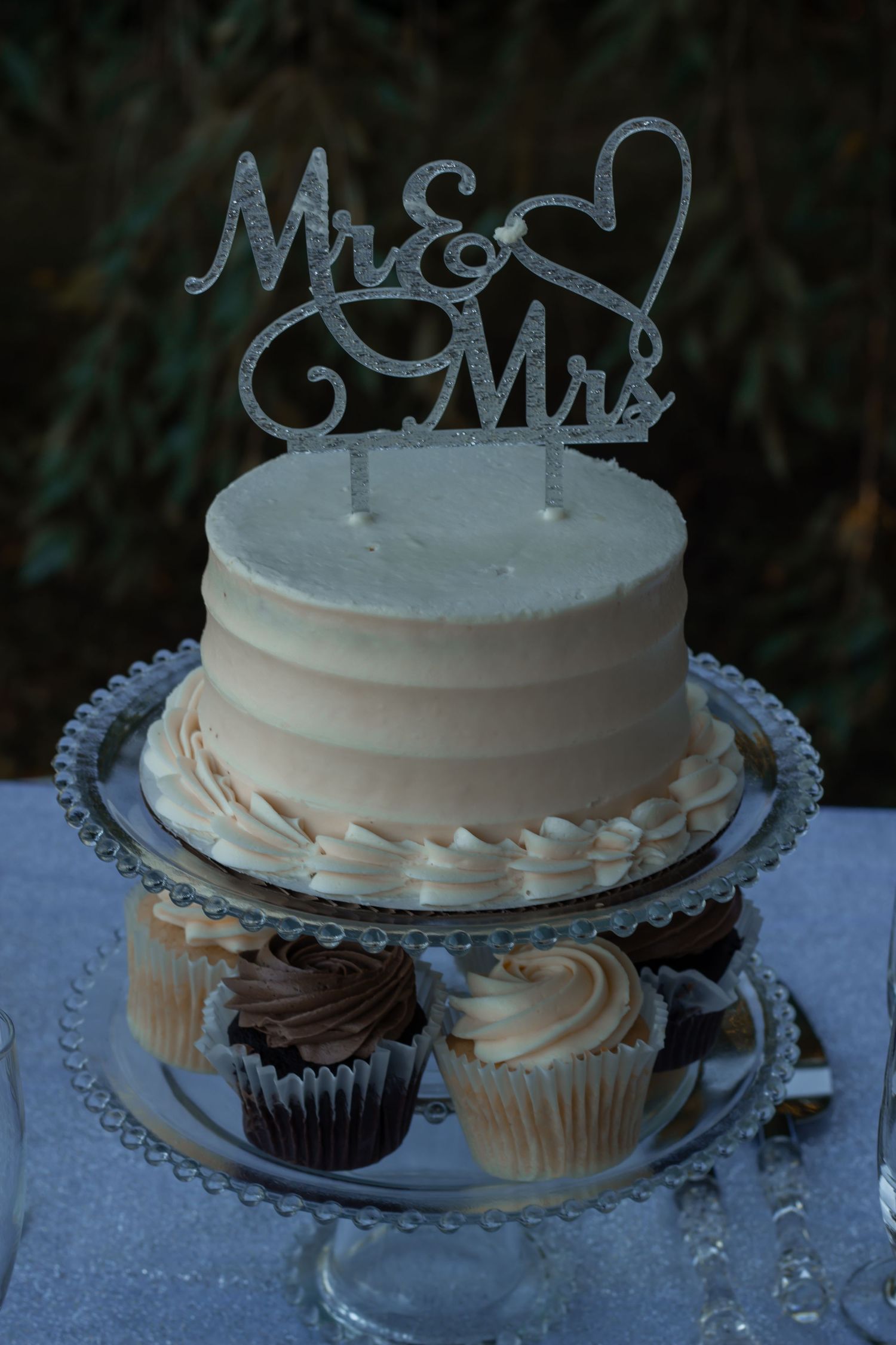 picture of wedding cake with mr & mrs sign. cupcapkes on bottom tier
