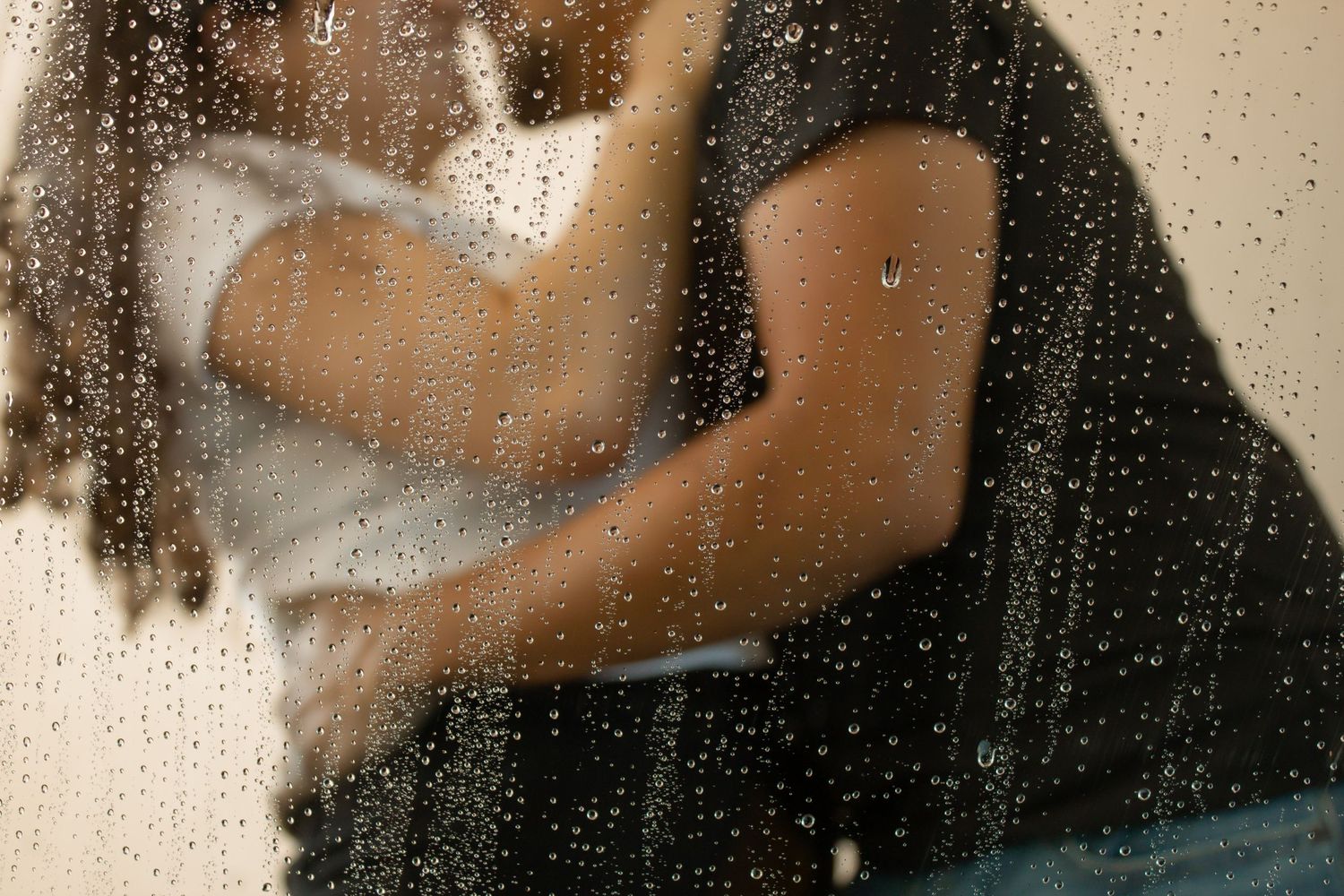 picture of couple kissing. the window of back of car with water.