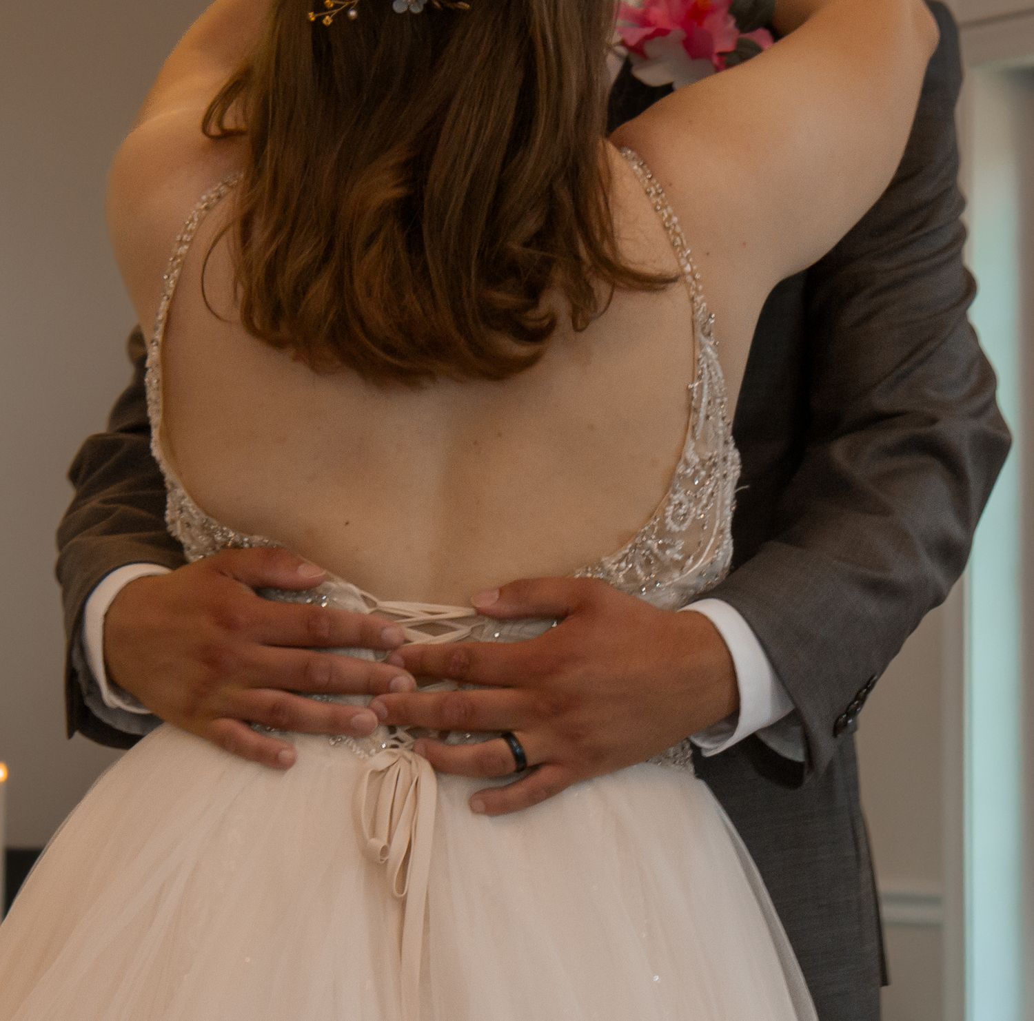 picture of bride and groom first dance. focal of bride's back and grooms hands around her waist, showing his ring.