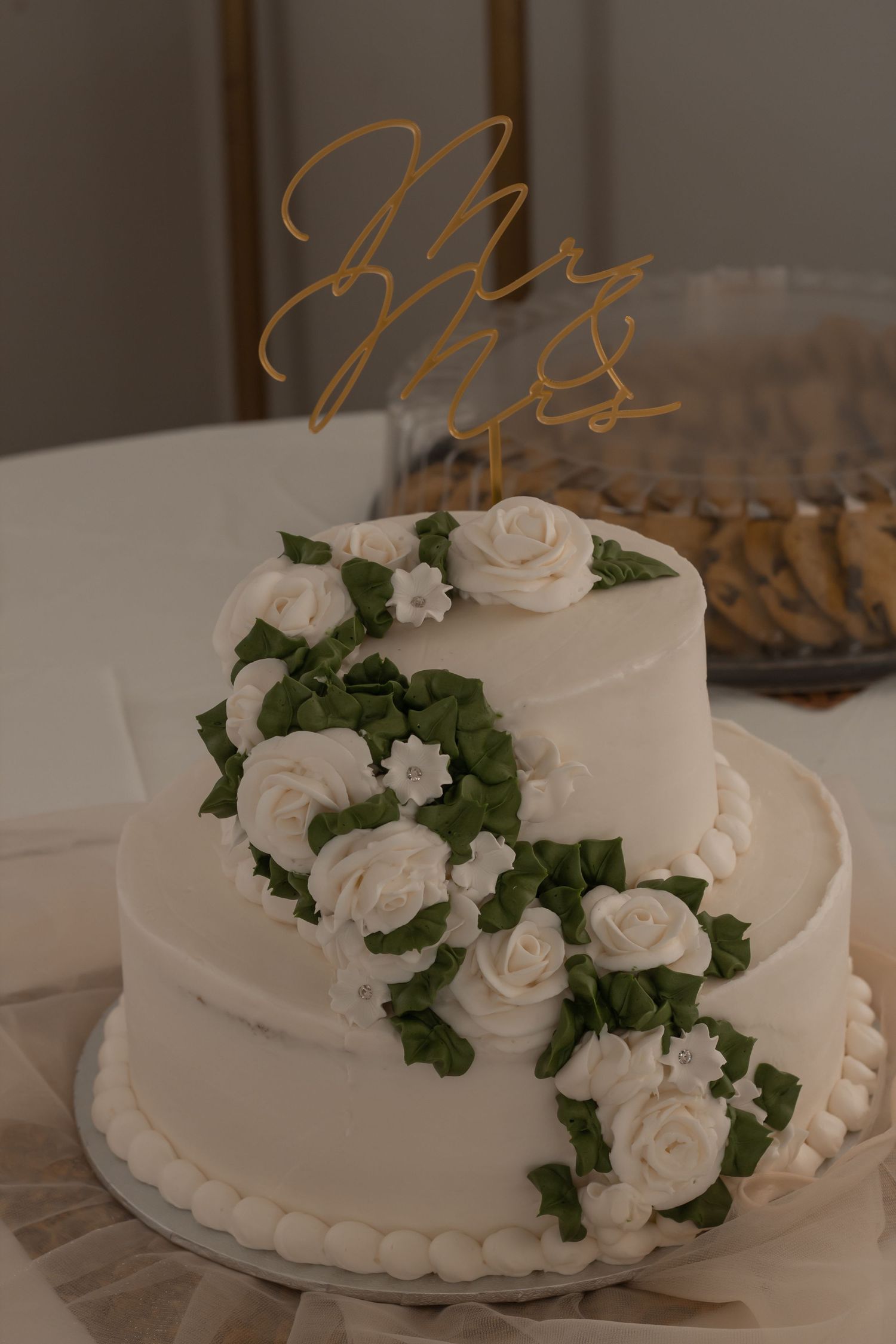 picture of  white wedding cake with white flowers and green garlands around cake leading up to top of cake.