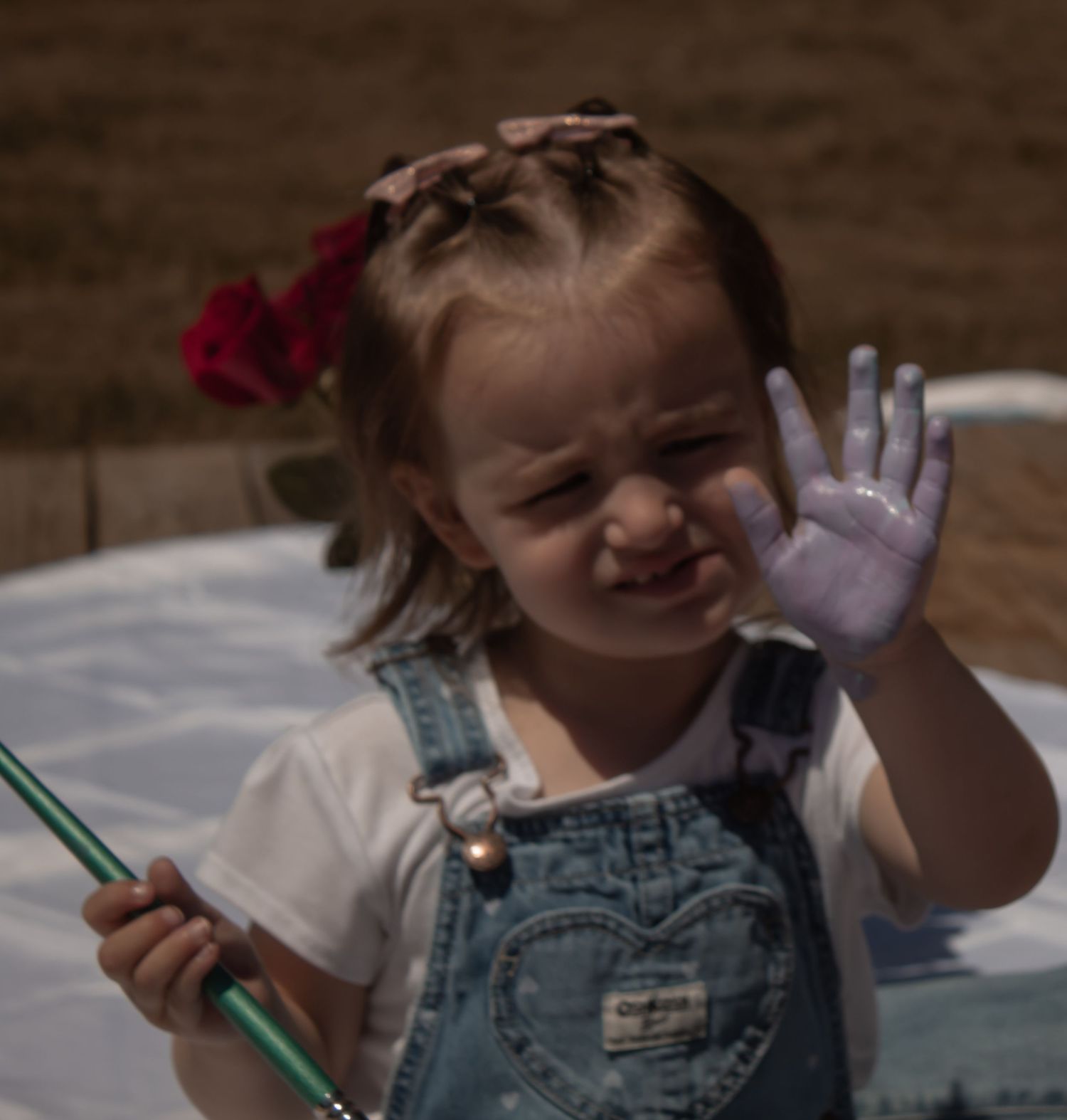 picture of toddler girl with her left palm full of purple paint. she's holding a brush on her right hand.
