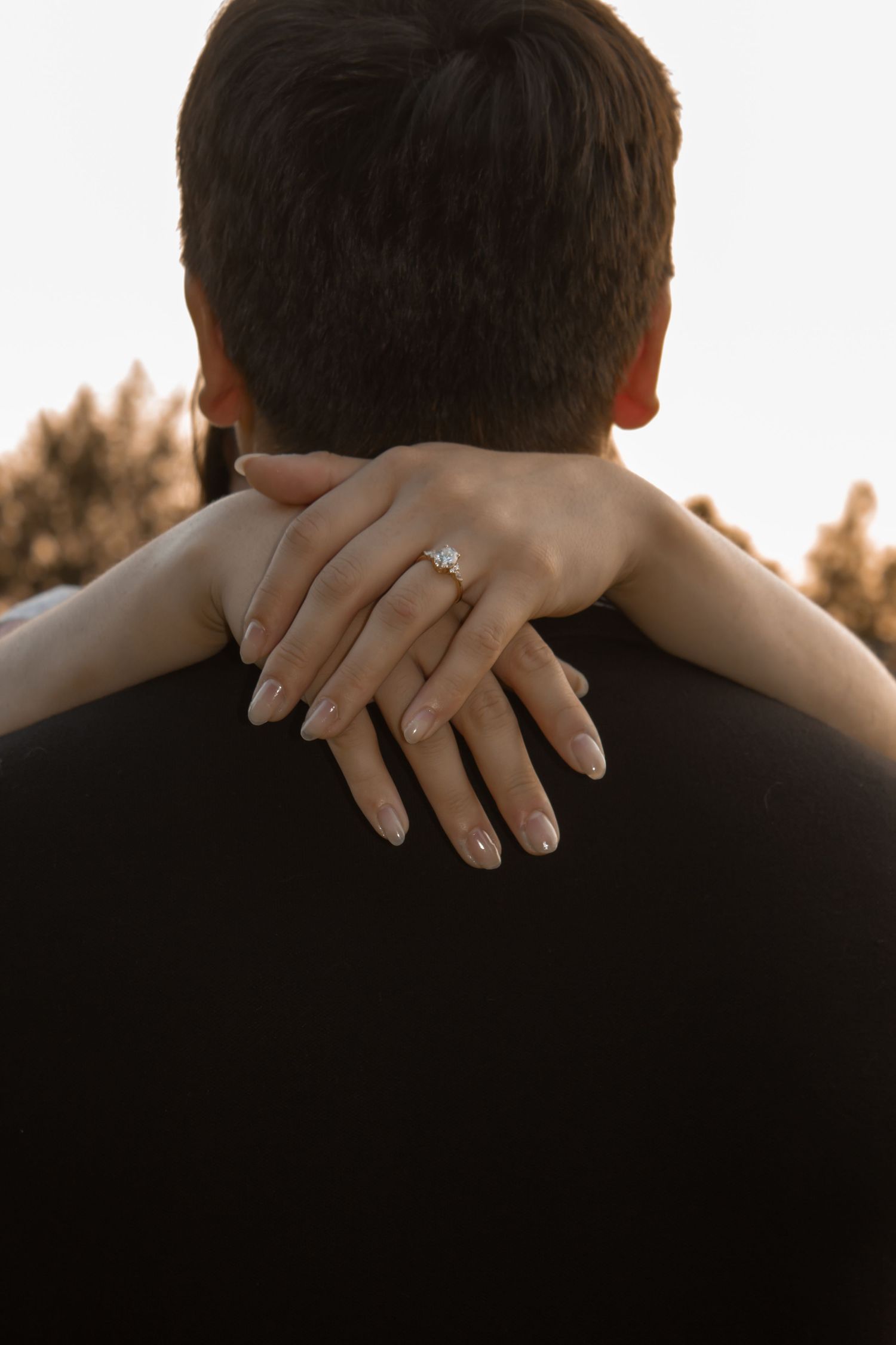 picture of couple session. back of guy and girls hands wrapped around his neck showcasing her ring.