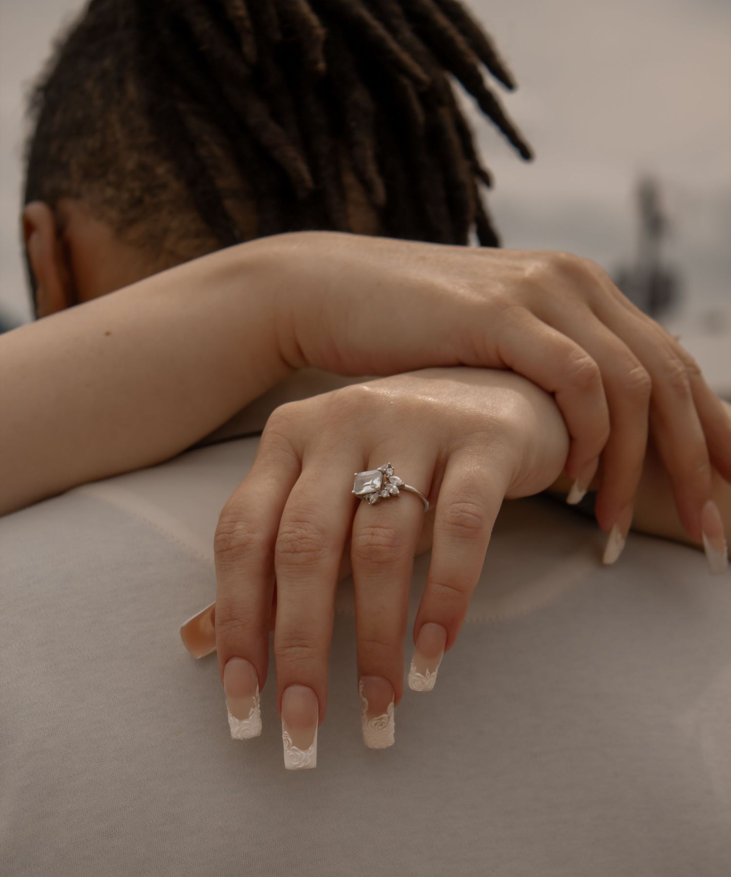 picture of couple at beach. focal point of girl holding her guy. focal point of her hands showcasing the ring. back of guys head