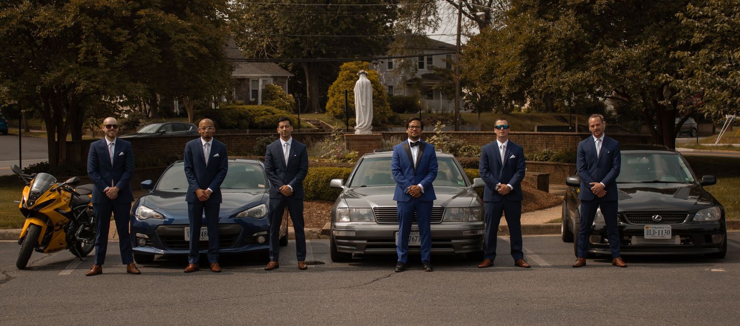 picture of all groom's mens lined up next to each other in front of their cars in parking lot