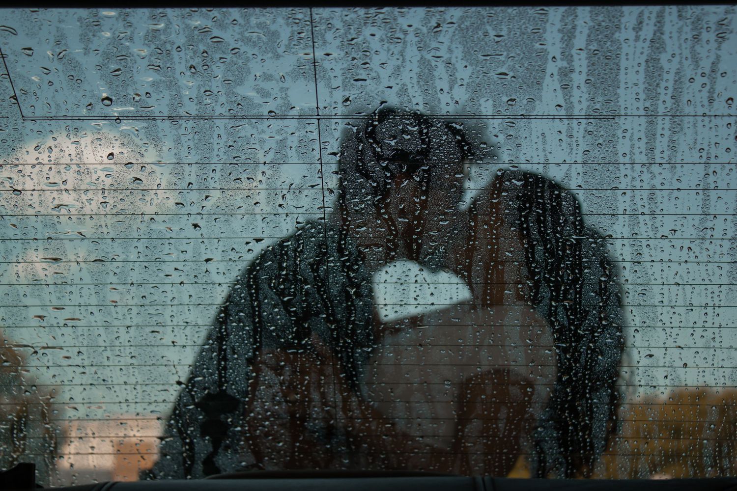 picture of couple kissing, the reflection of them in car with rain or water on window shield