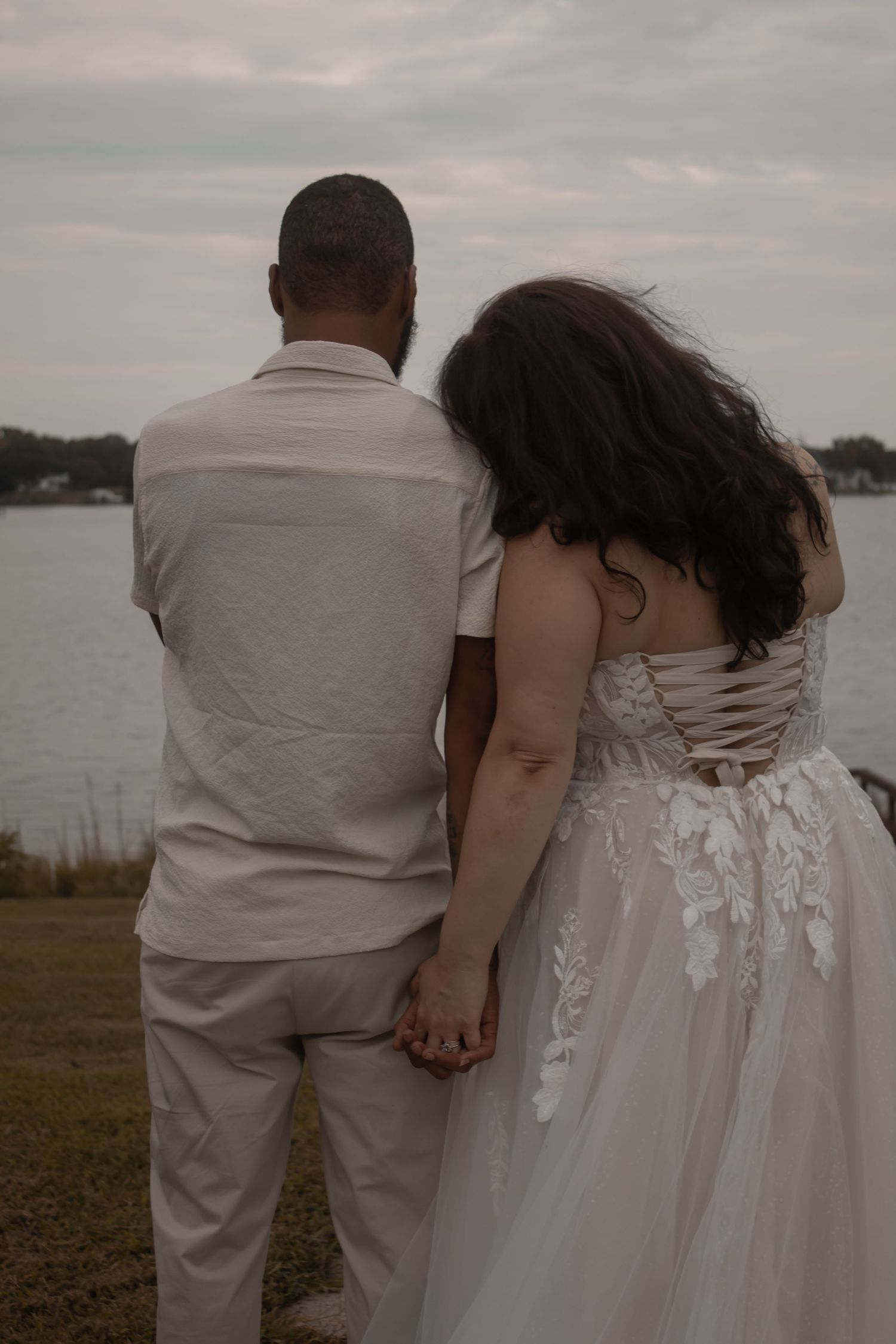 picture of couple at beach and dock, back of couple, looking at beach, girl leaning her head on guy's shoulder.