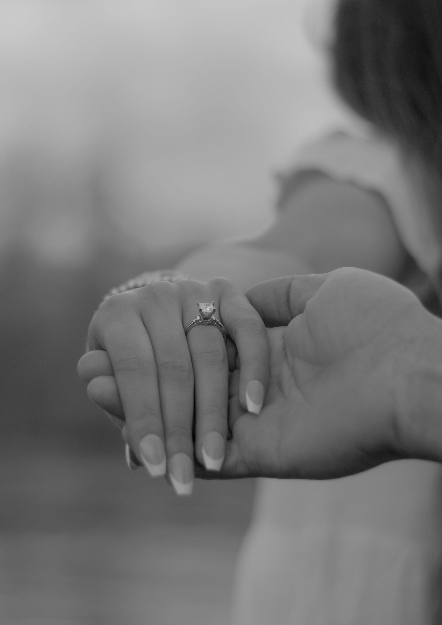 picture of girl's hand in black and white show casing the engagement ring. the man is holding her hand showing off her new ring.