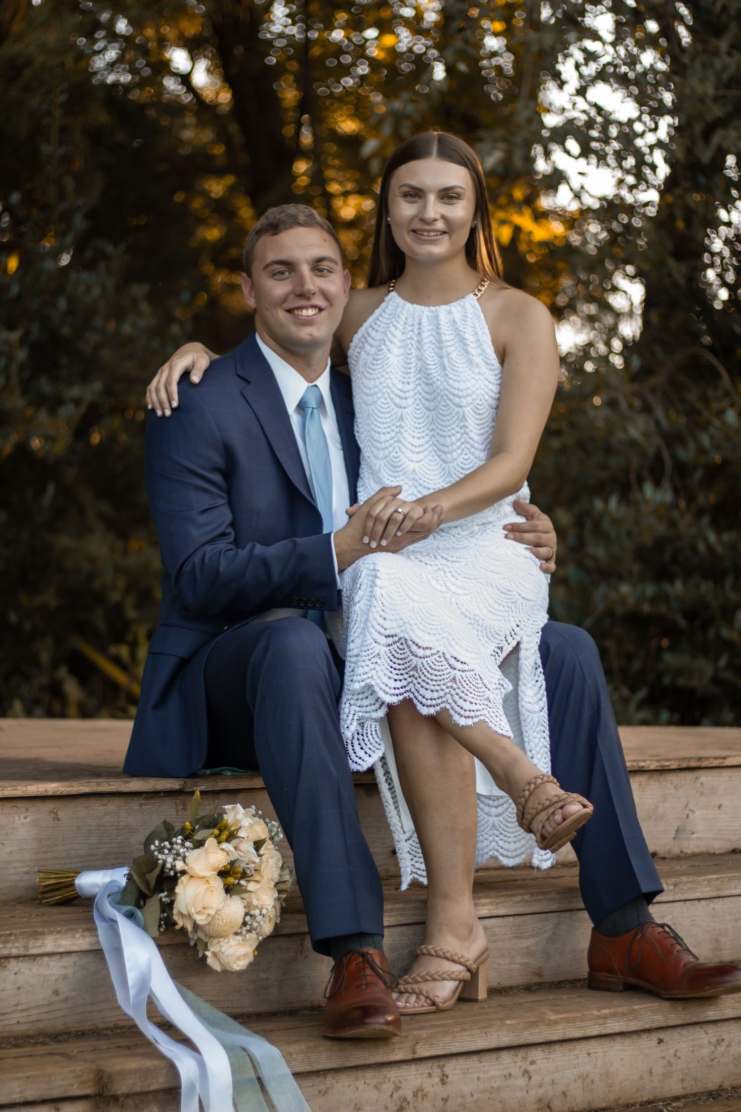 picture of couple sitting on bench after they just got married, both holding each other's hand.