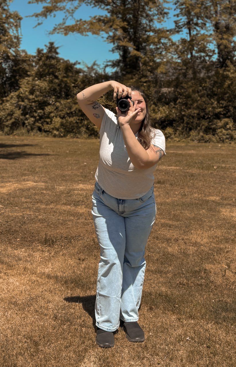 picture of amber dunnigan in forest, holding camera up to her face as if she's about to snap pictures of you