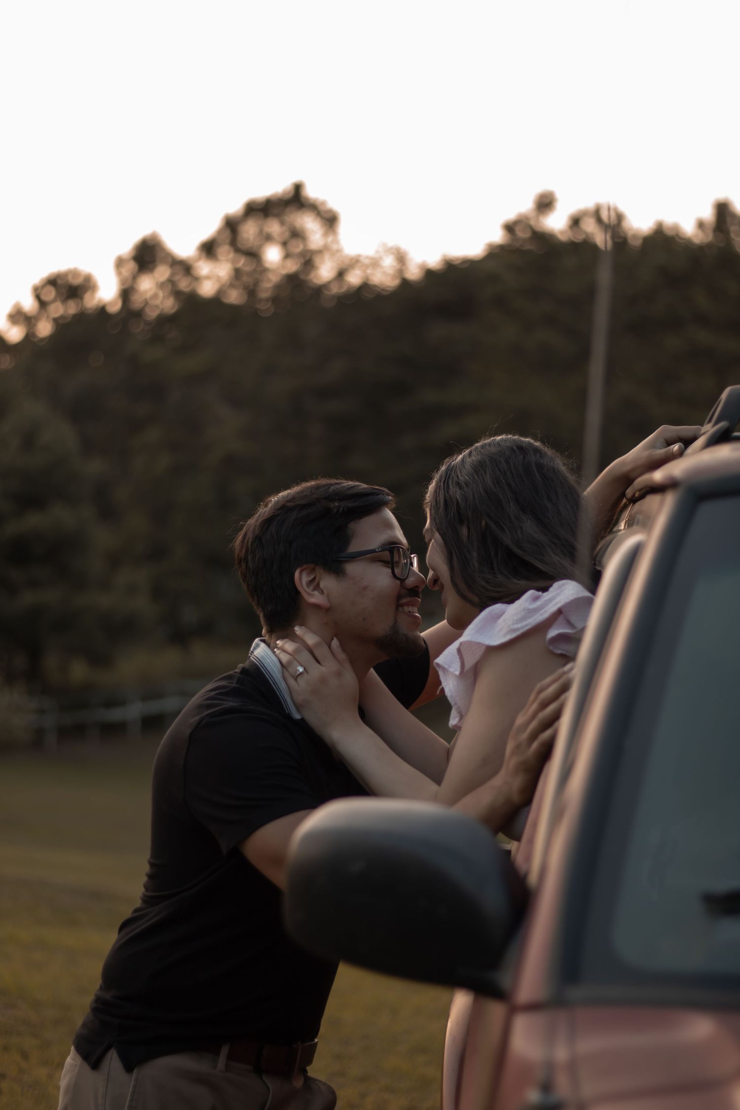 picture of couple, engagement,  girl in the car, sticking out of window and the guy is standing outside the car and they're about to kiss