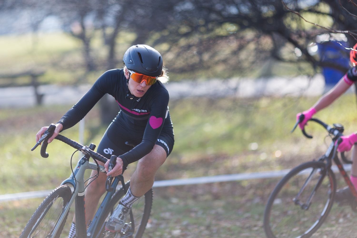 Female cyclist in black kit races on a cyclocross bike through an open field on a clear winter day.