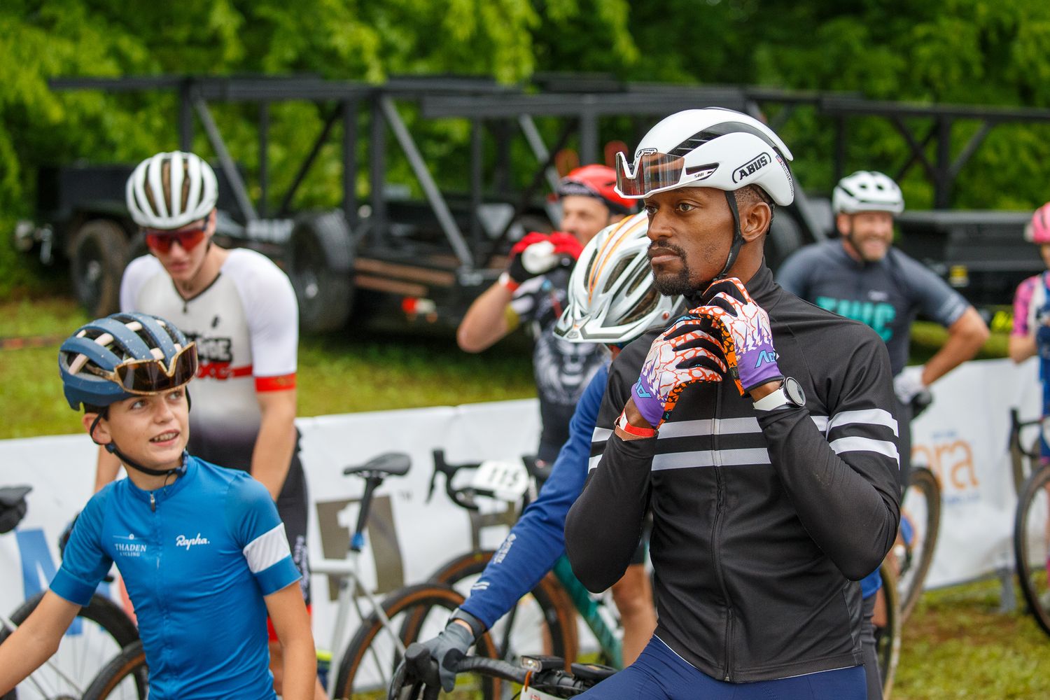 Cyclists in helmets gather at an outdoor cycling event on a cloudy day.