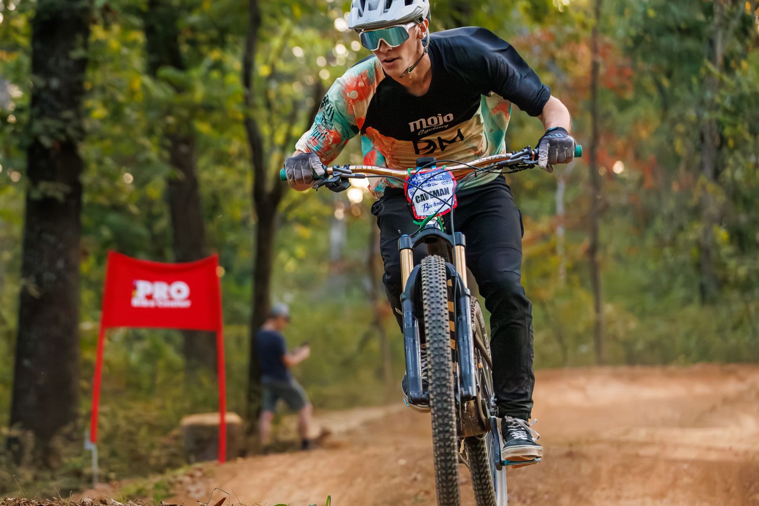 Mountain biker in helmet and tattoos races down dirt trail during outdoor cycling competition.