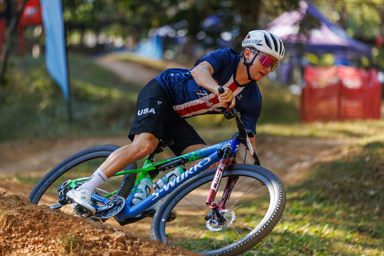 USA team mountain biker aggressively cornering on a dirt trail during a competitive race.
