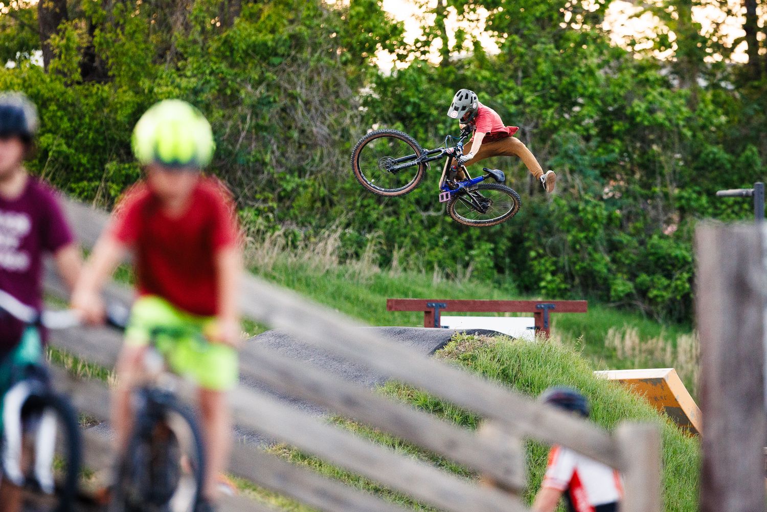Mountain biker soars through the air at a pump track while spectators watch in the foreground.