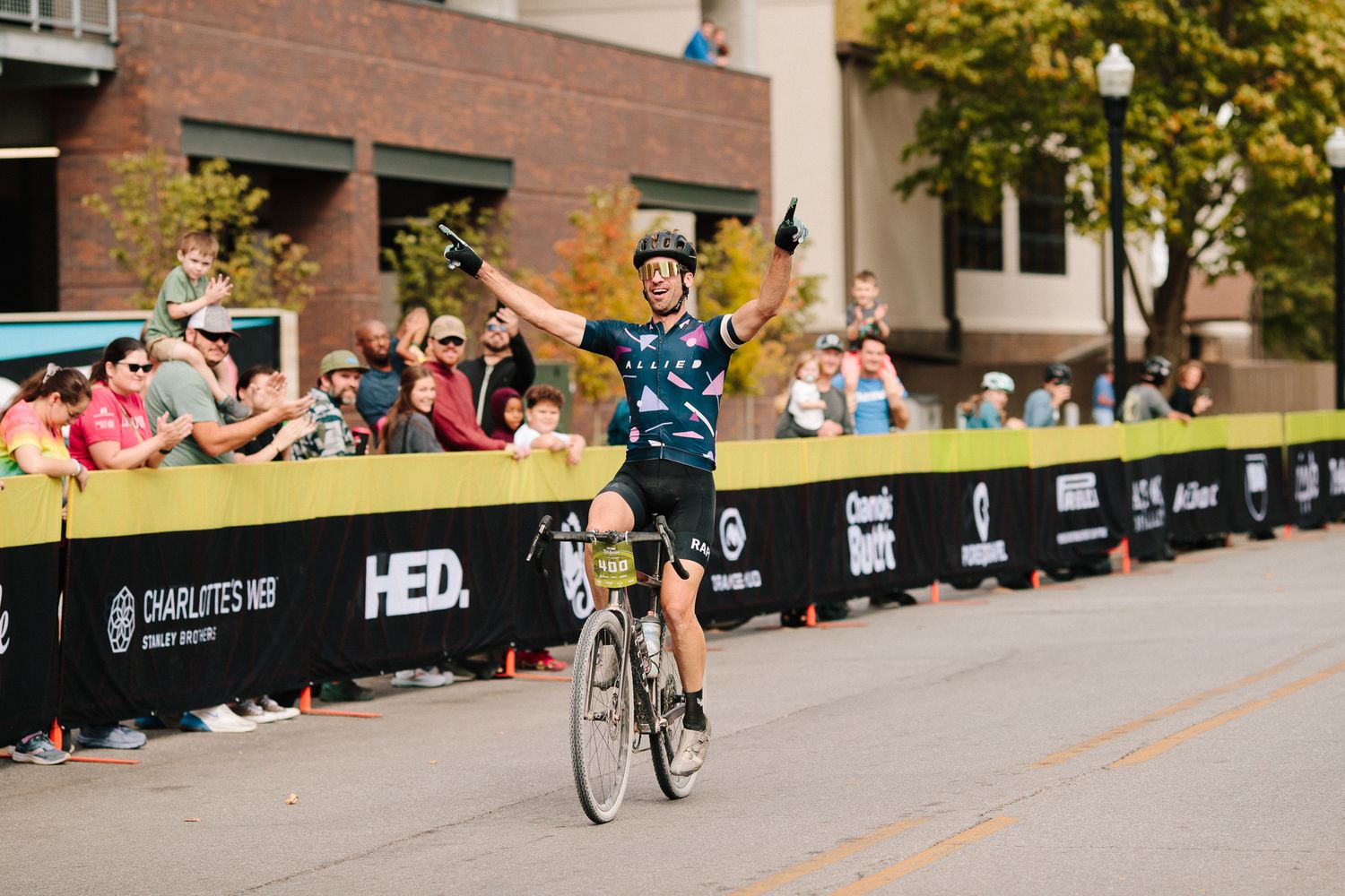 Triumphant cyclist raises both arms crossing the finish line at an urban cycling race event.