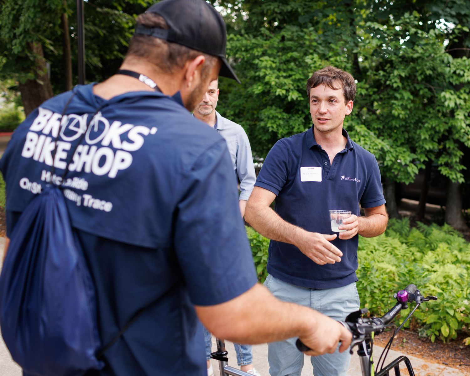 Men in casual attire conversing outdoors near a bicycle at a bike shop event.