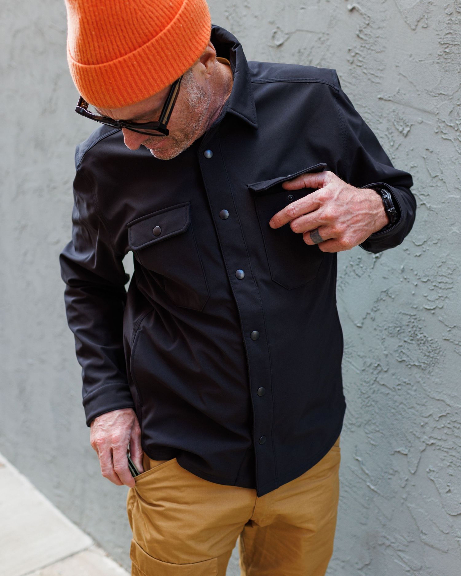 Man in orange beanie demonstrating black snap-button shirt jacket features.