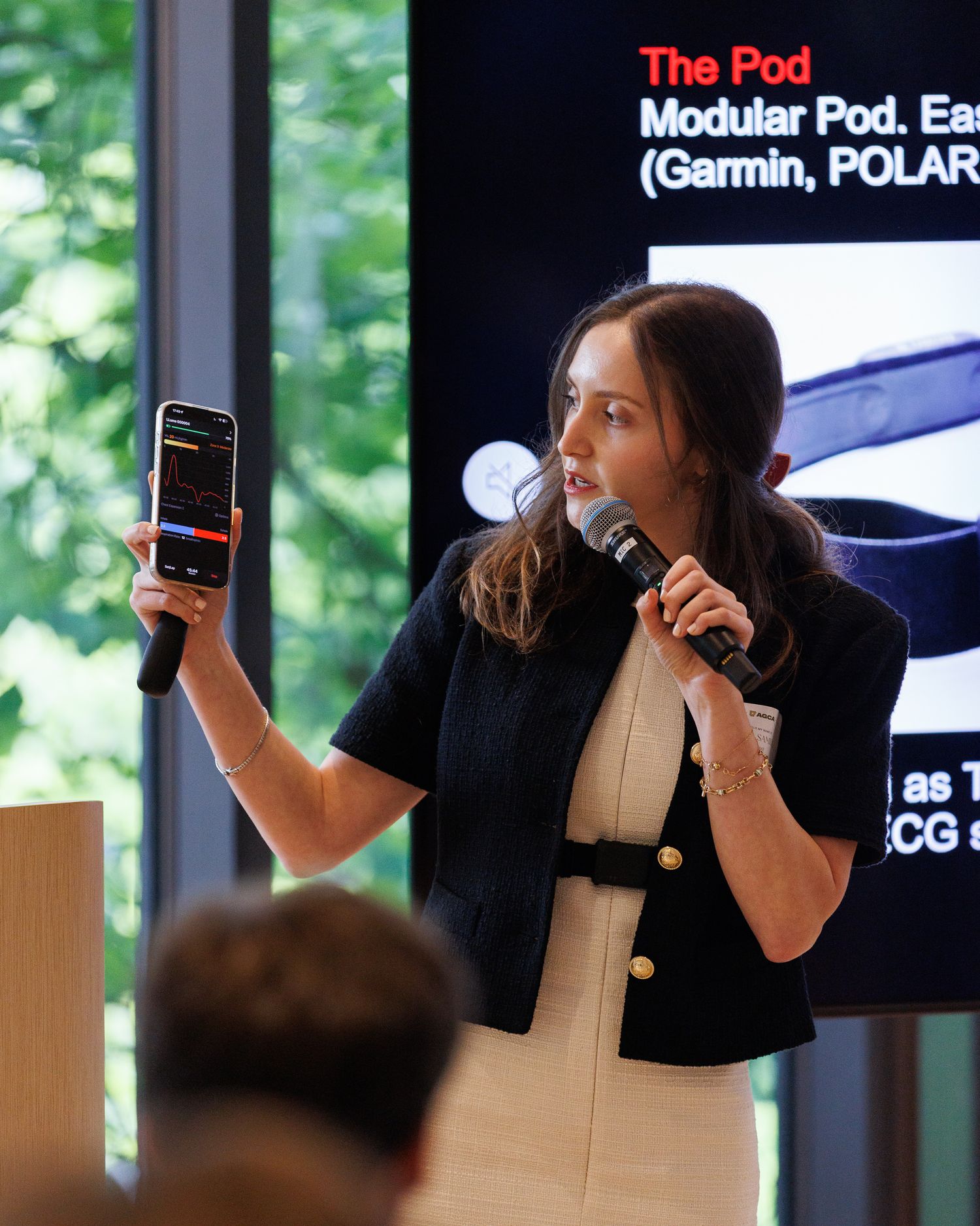 Woman presenting a smartphone app and speaking into a microphone at a cycling technology event.