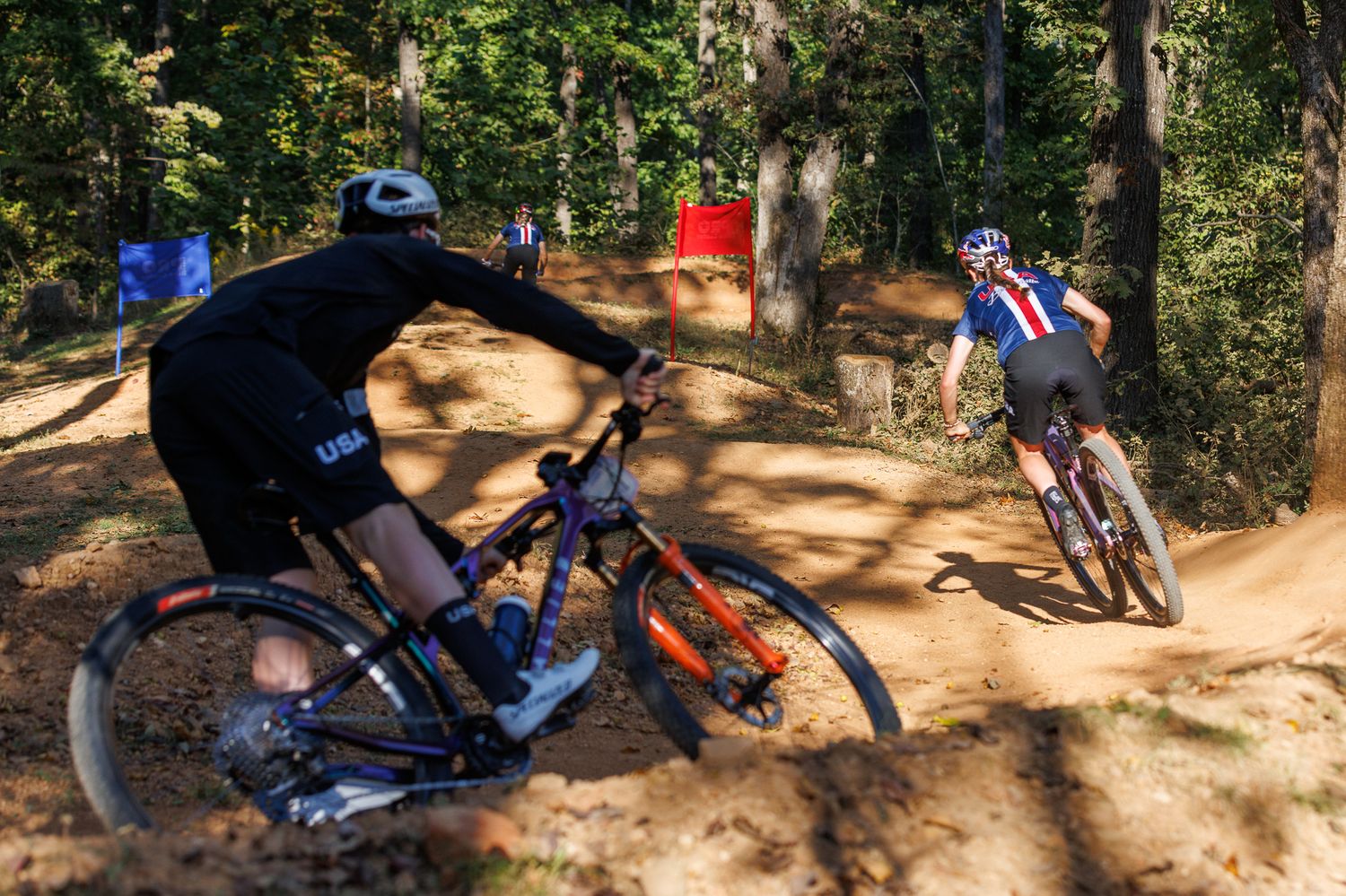 Two mountain bikers navigating a dirt trail through a wooded forest during a race.