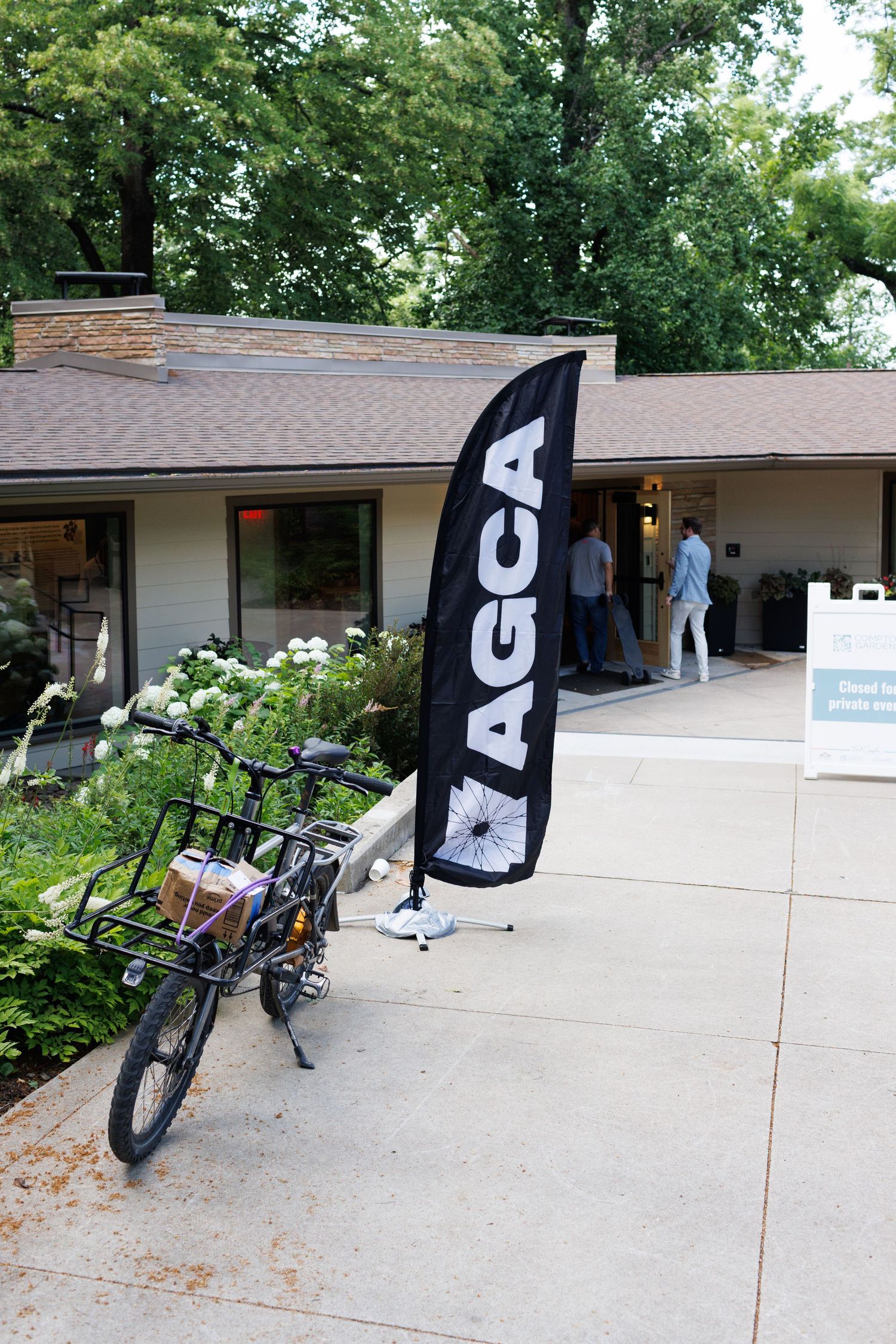 AGCA branded flag banner beside a parked cargo bike outside a mid-century modern building.