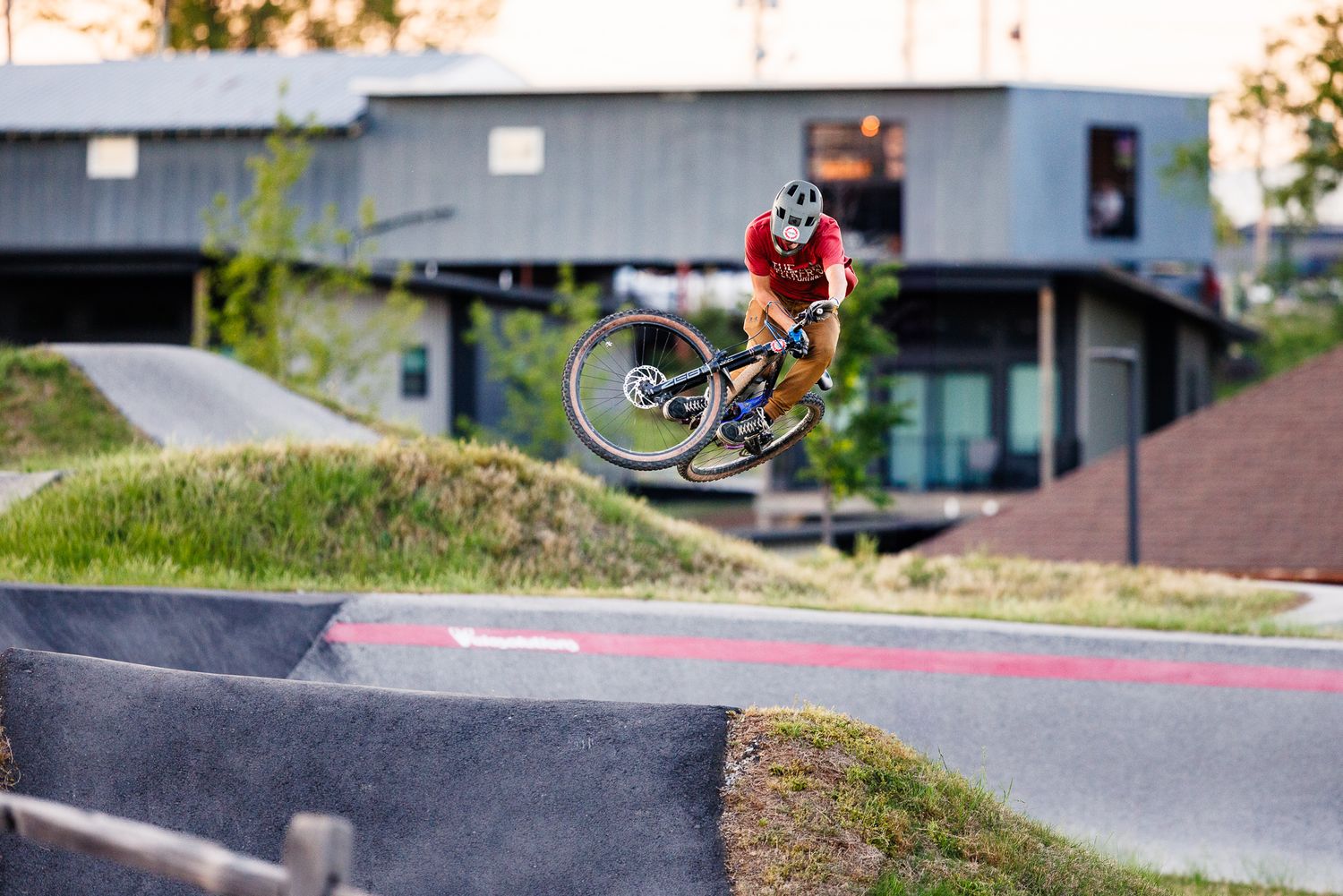 Aerial mountain bike trick performed at a professional pump track park during golden hour lighting.