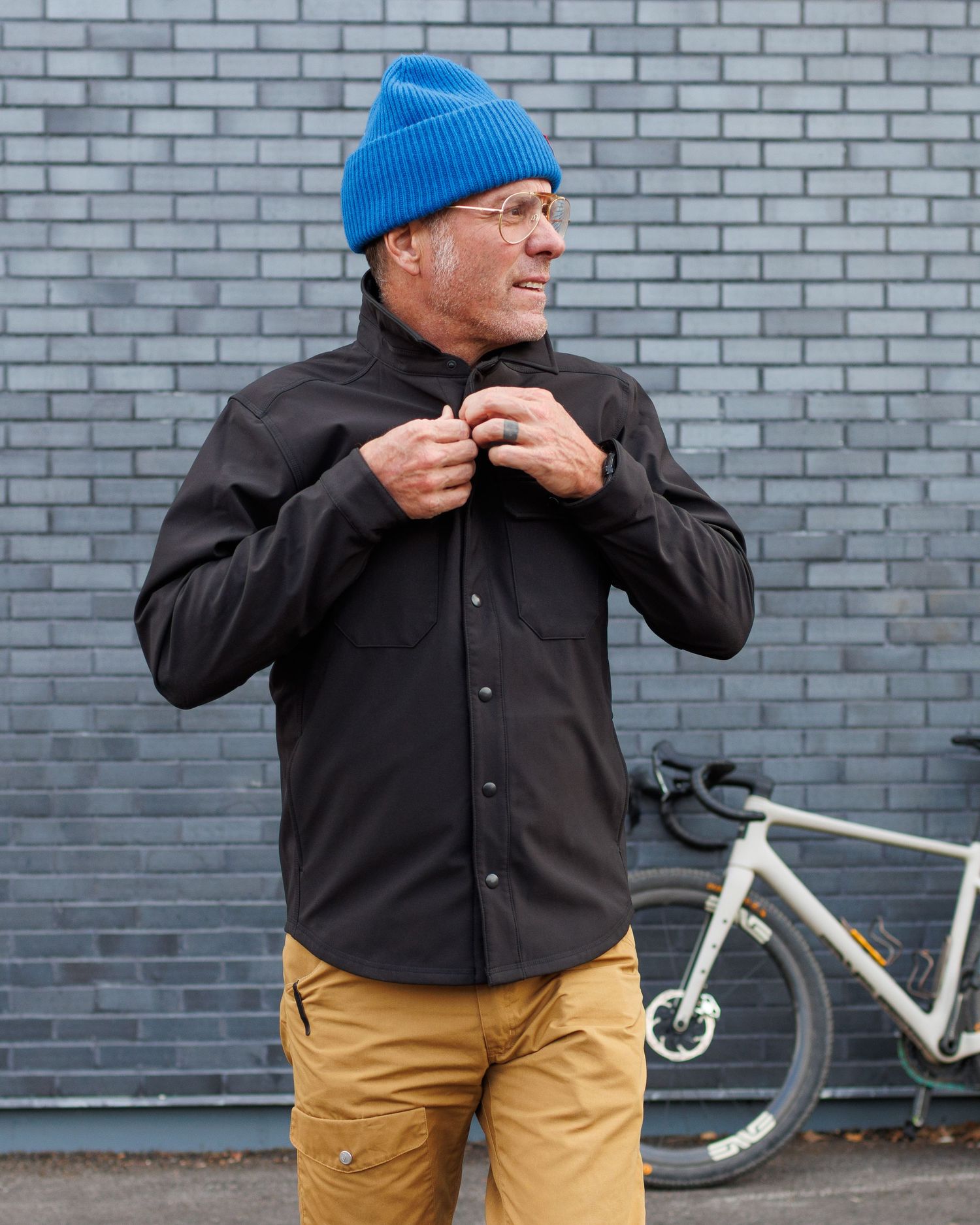 Man in blue beanie zipping black technical shirt jacket outdoors.