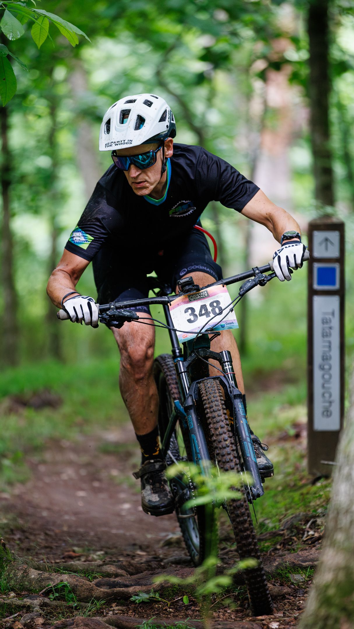 Mountain biker wearing number 348 racing on a wooded trail during a cycling competition.