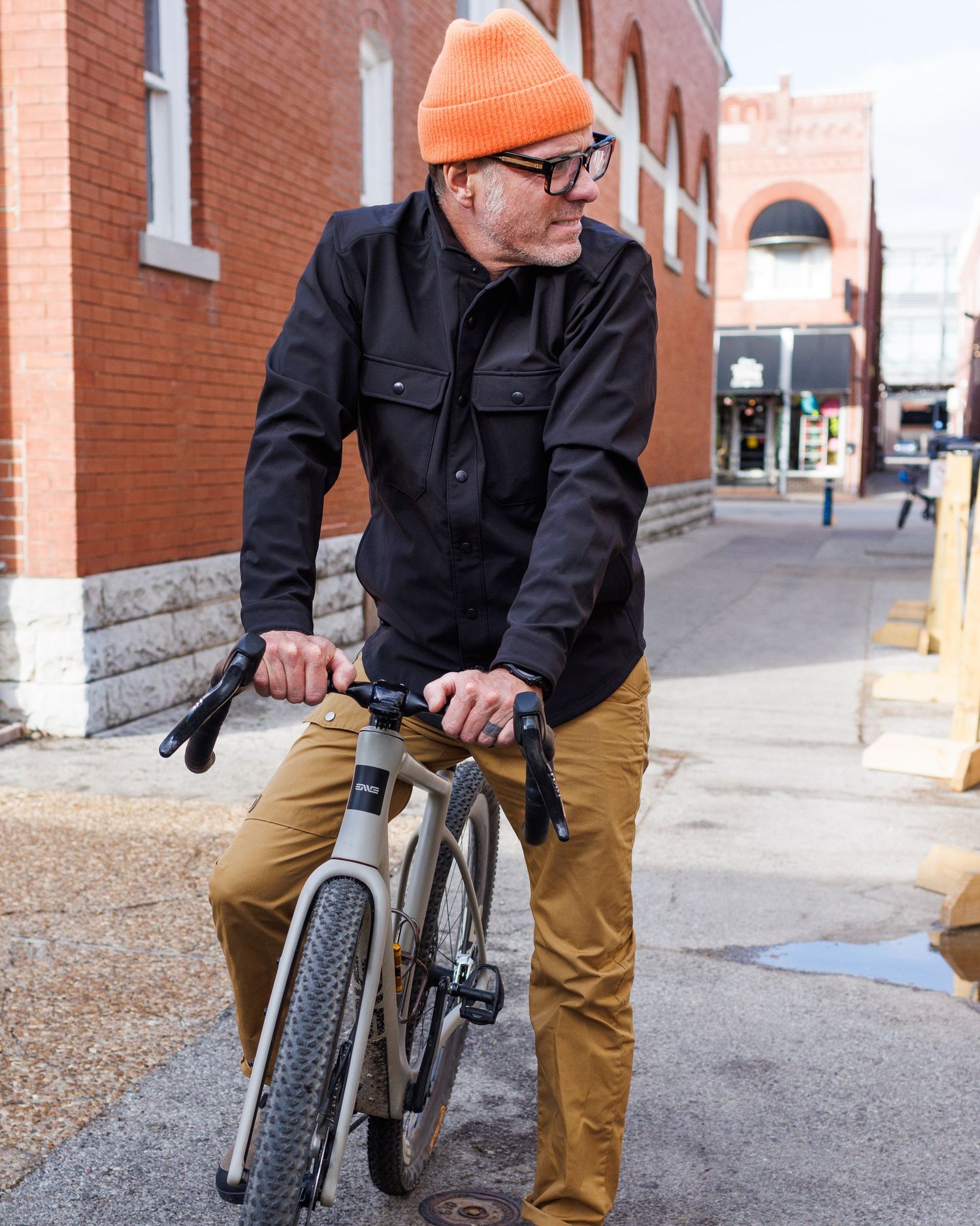 Man in orange beanie riding bicycle on urban street.