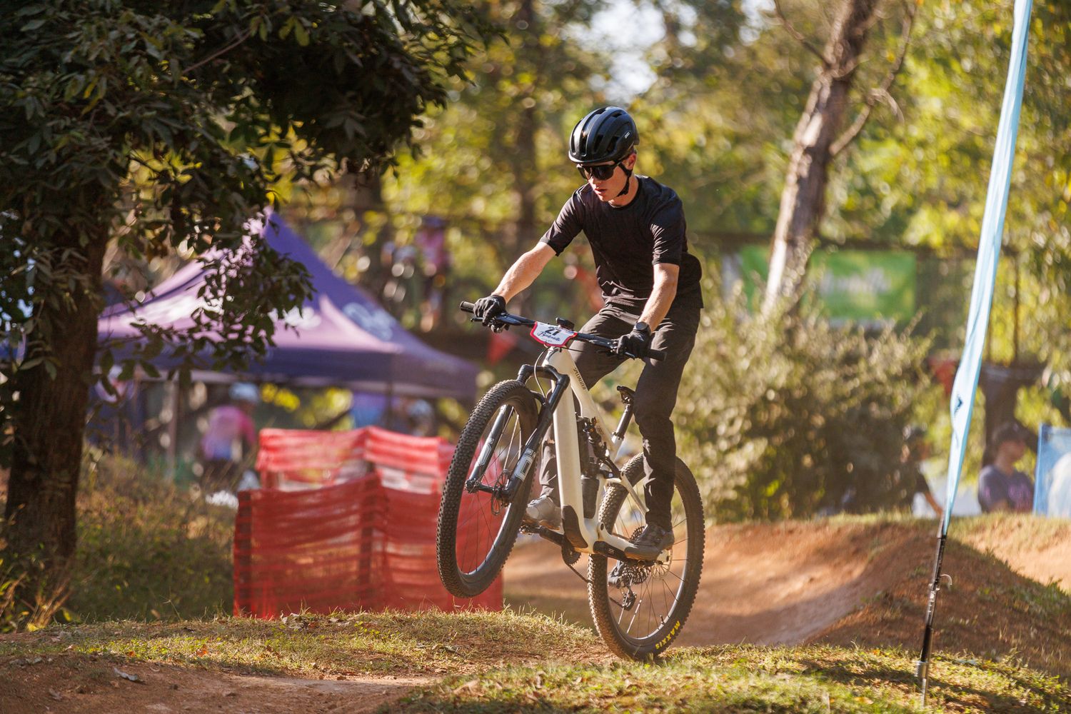 Female mountain biker riding through a dirt trail in a wooded area during a race.