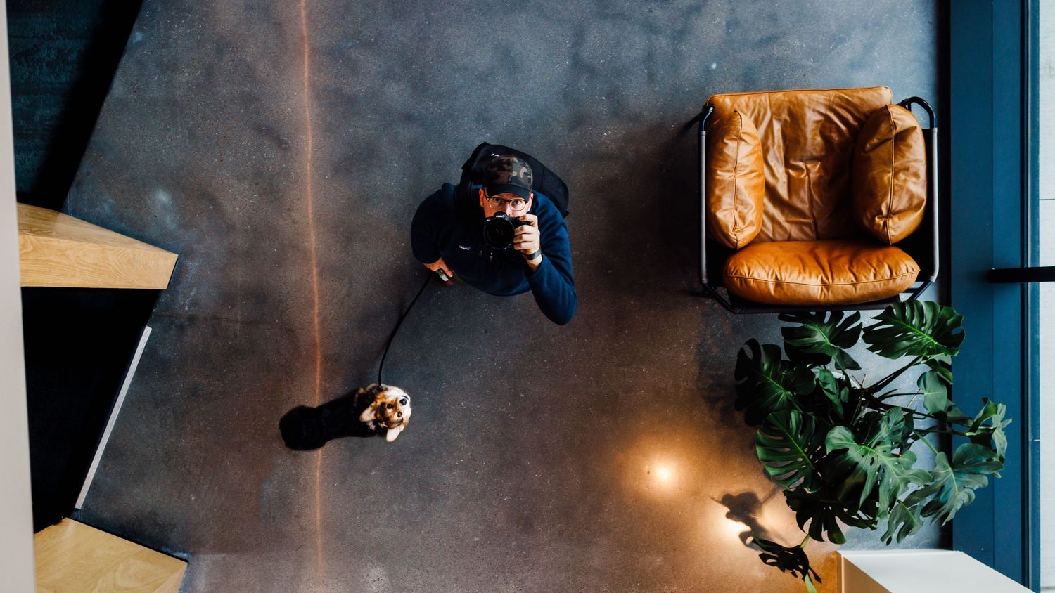 Aerial view of a person sitting on a concrete floor near a leather chair and plant.